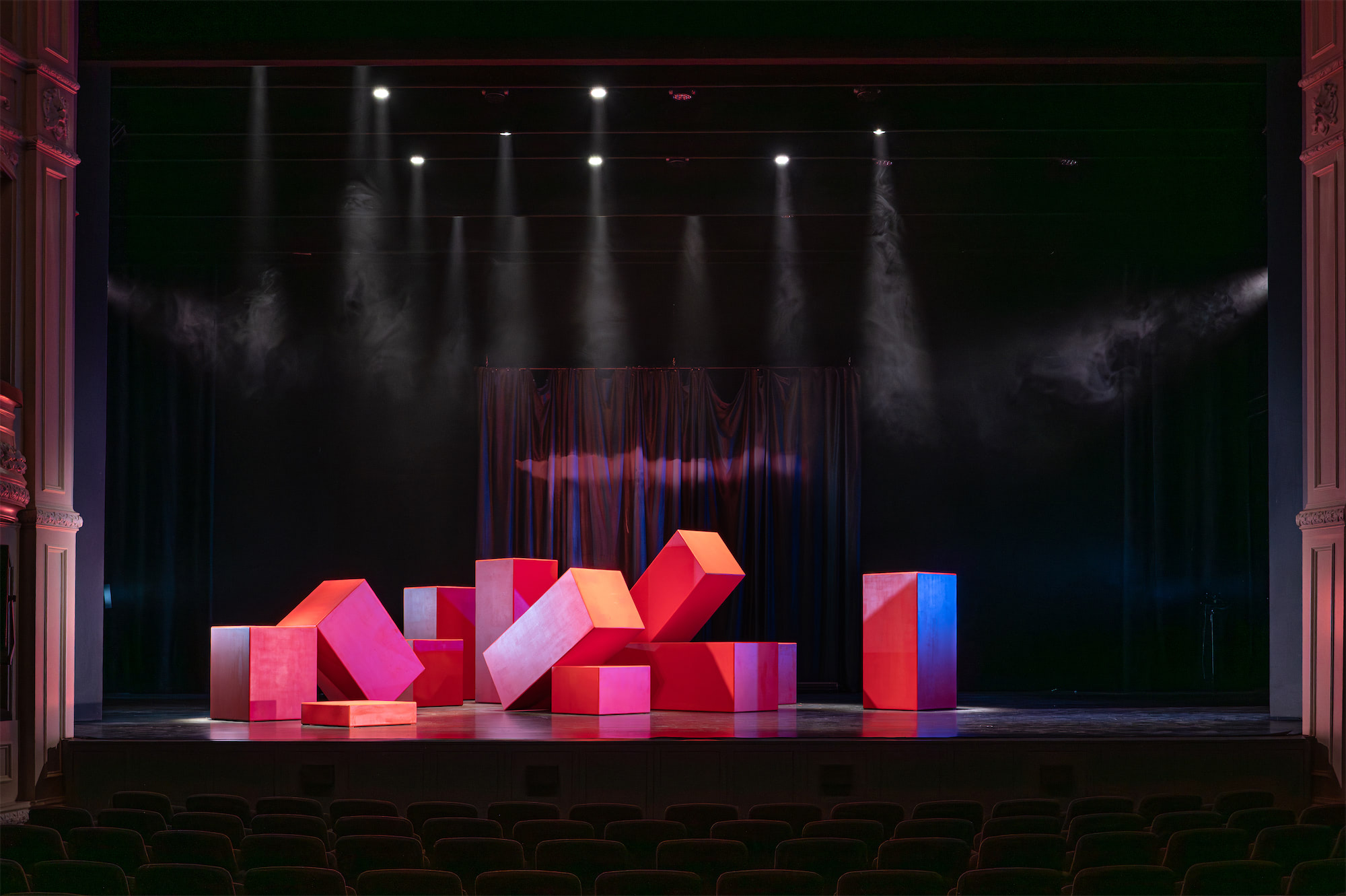 een theatervloer met en berg met grote oranje blokken kriskras door en over elkaar liggend.