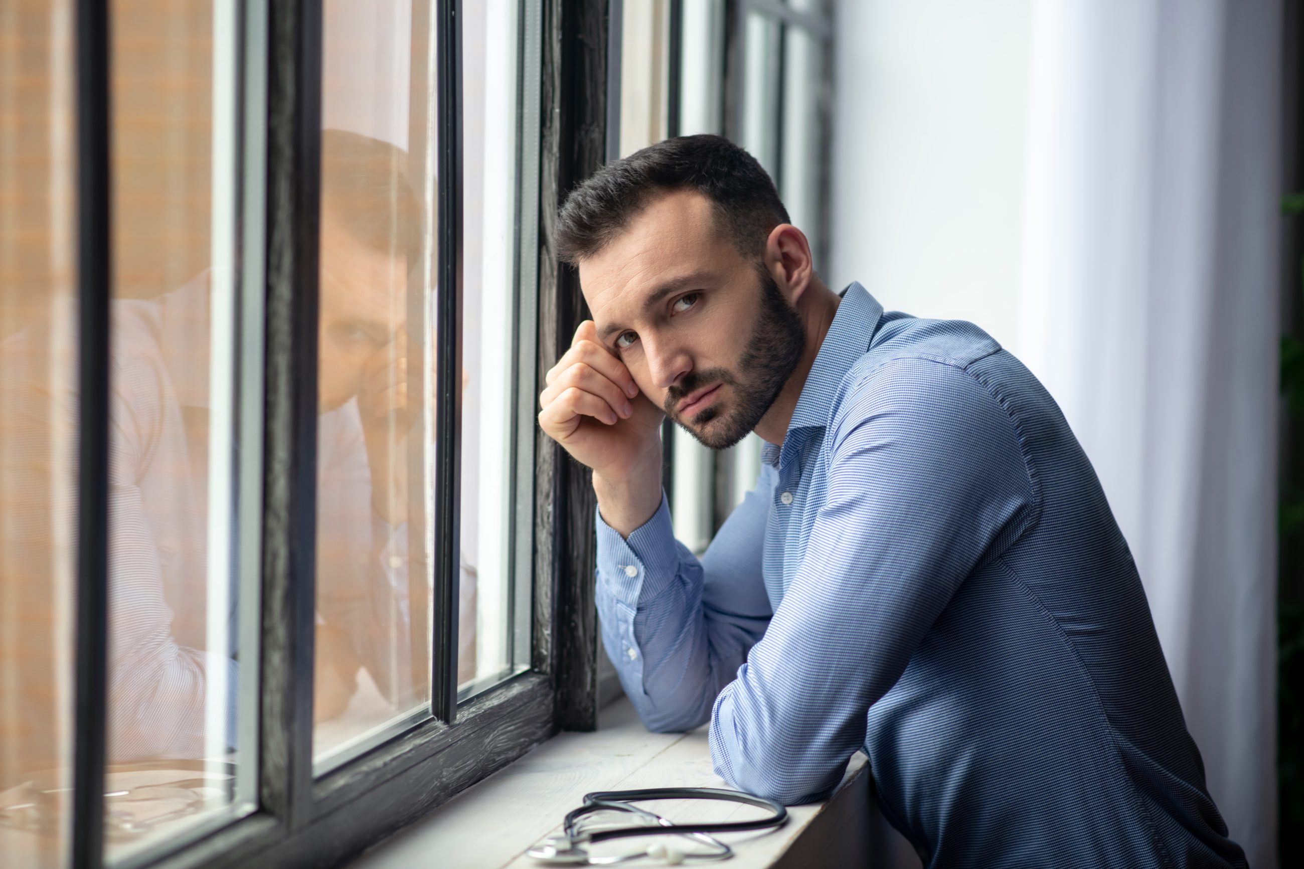 Nachdenklicher Mann am Bürofenster, Sinnbild für Boreout und Unterforderung im Job