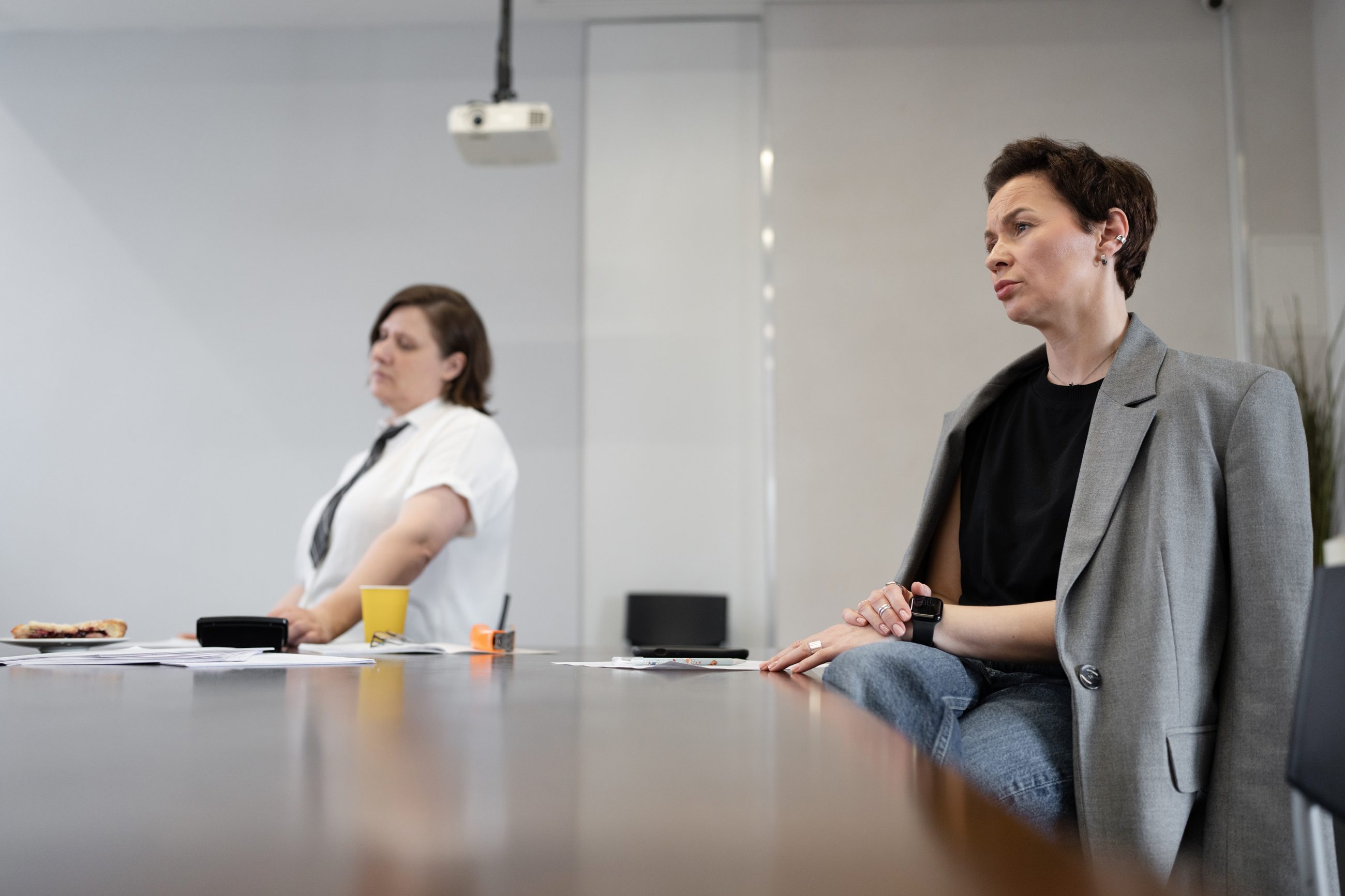 Zwei Kolleginnen sitzen schweigend am Konferenztisch, ohne Blickkontakt, Sinnbild für vermiedene Gespräche