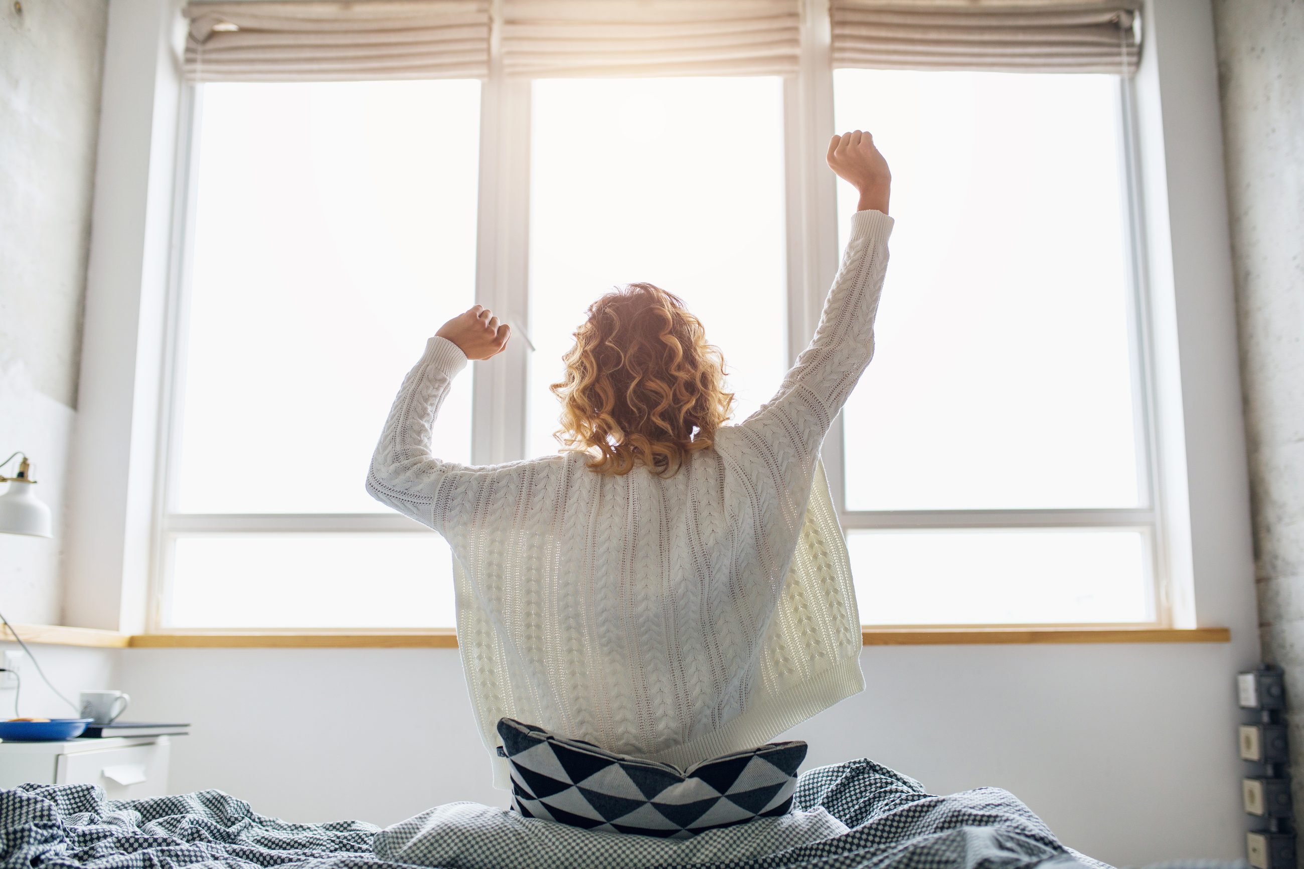 Frau streckt sich morgens am Fenster nach dem Aufwachen