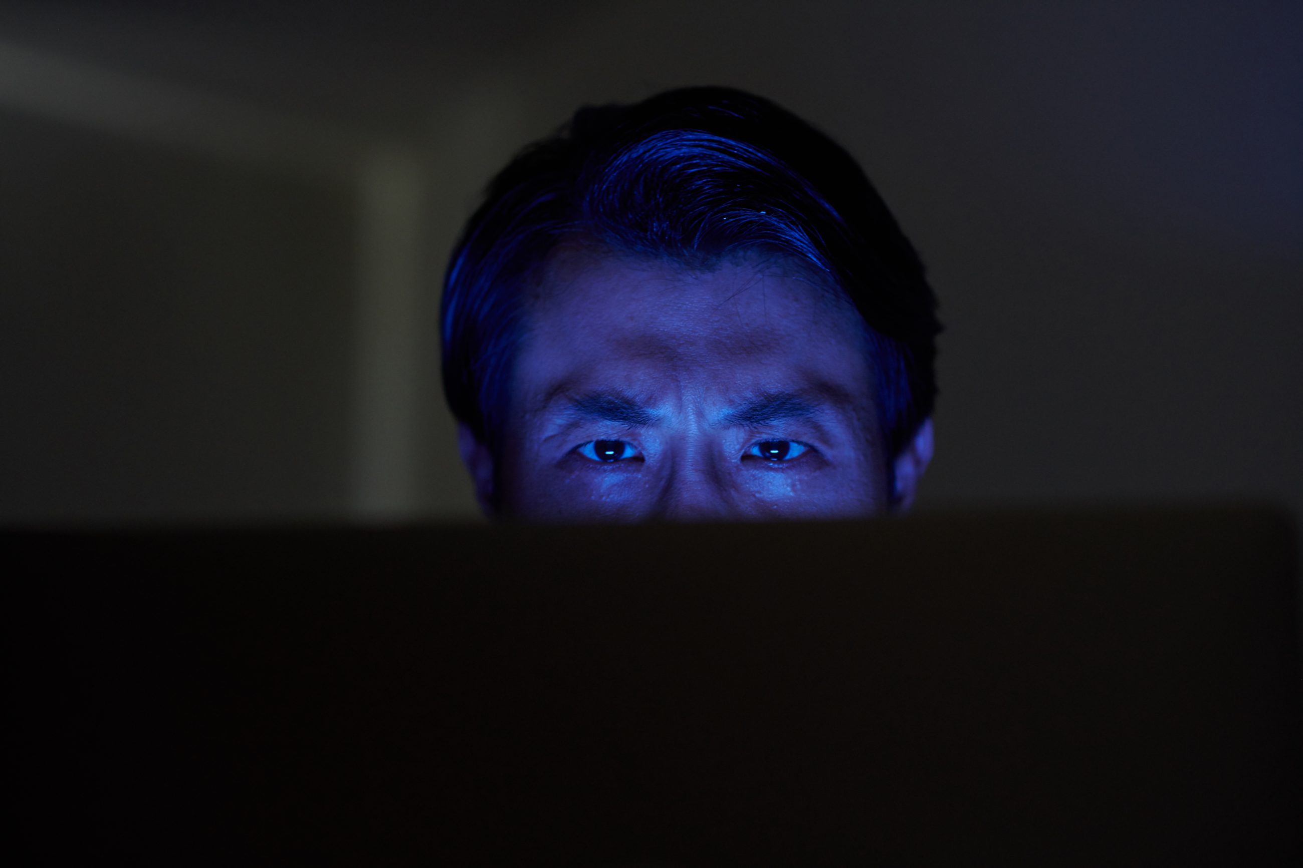 Person vor einem Laptop-Bildschirm im Dunkeln, Gesicht blau beleuchtet – Symbolbild für KI-gestützten Bewerbungsbetrug im Video-Interview