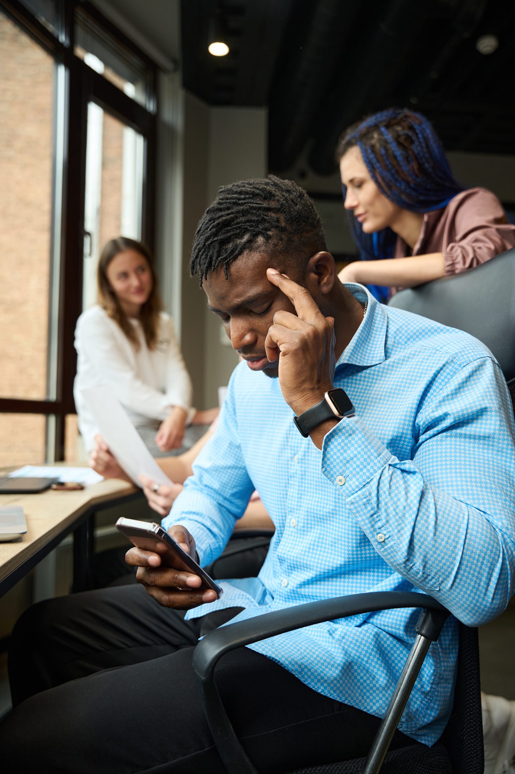 Mann prüft gestresst sein Smartphone während eines Meetings im Büro