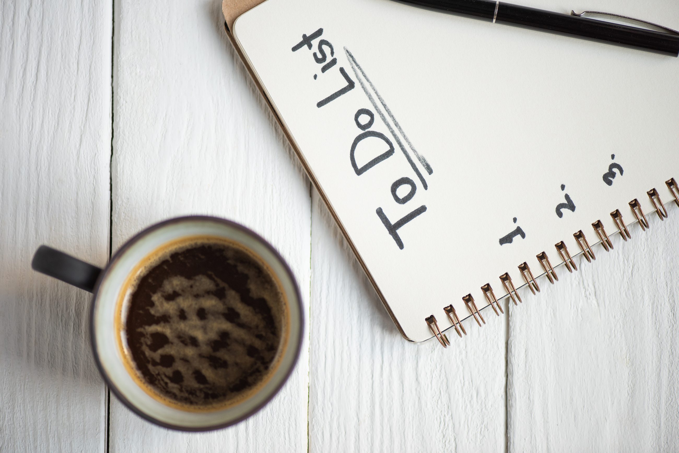 Handgeschriebene To-do-Liste in einem Notizbuch neben einer Tasse Kaffee, Symbolbild für unsichtbare mentale Verantwortung im Alltag