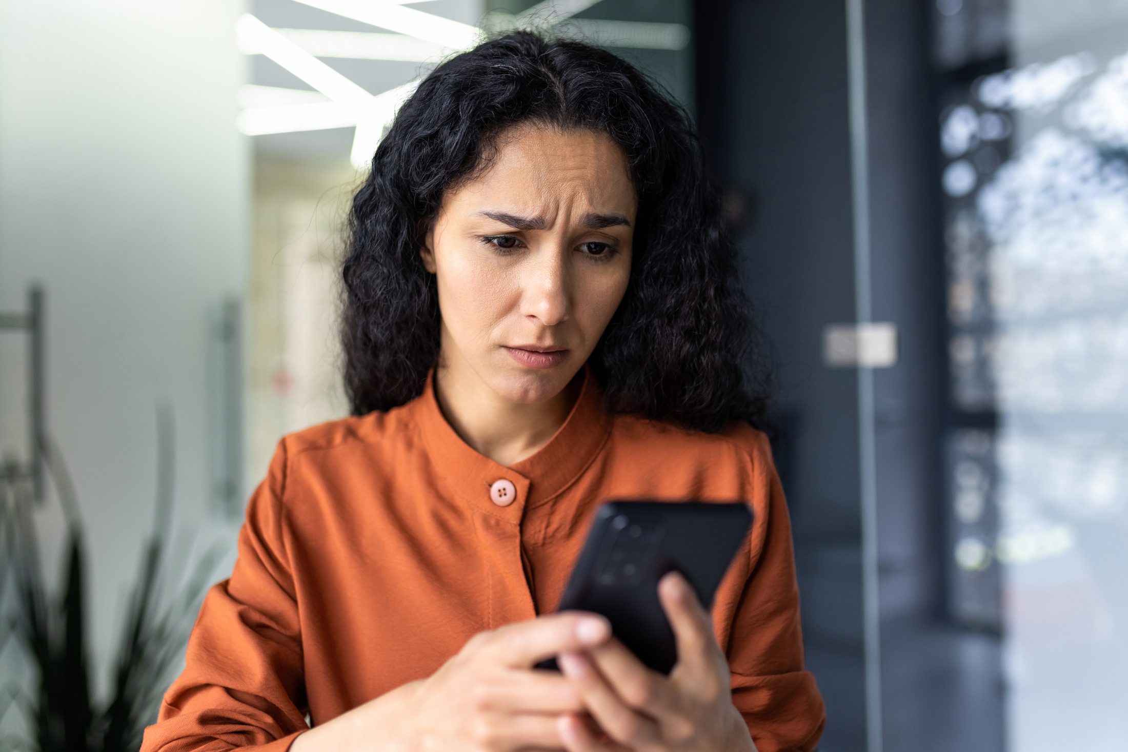 Frau blickt verwirrt und besorgt auf ihr Handy, nachdem eine Nachricht falsch bei ihr ankam – schriftliche Kommunikation und Missverständnisse
