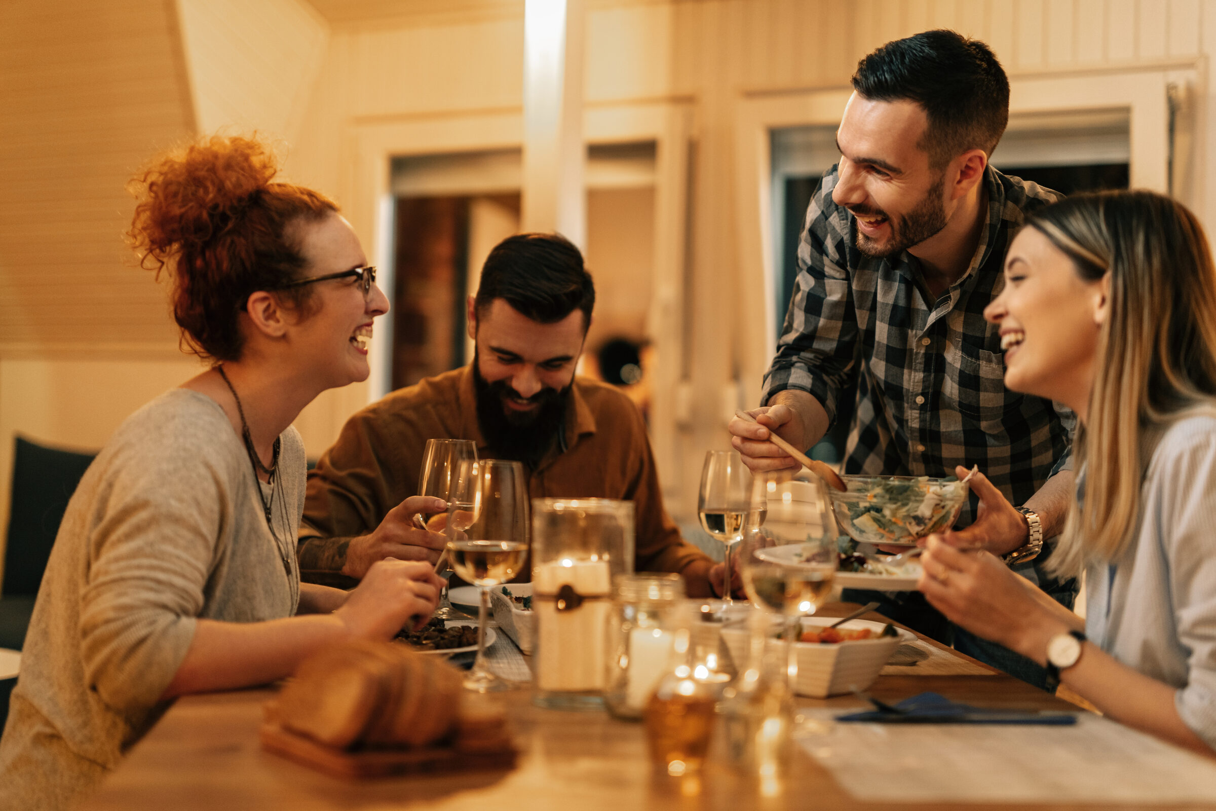 Gruppe von Freunden lacht gemeinsam beim Abendessen zuhause – Symbolbild für regelmäßige, absichtlich eingeplante Zeit als Basis echter Freundschaften im Erwachsenenalter