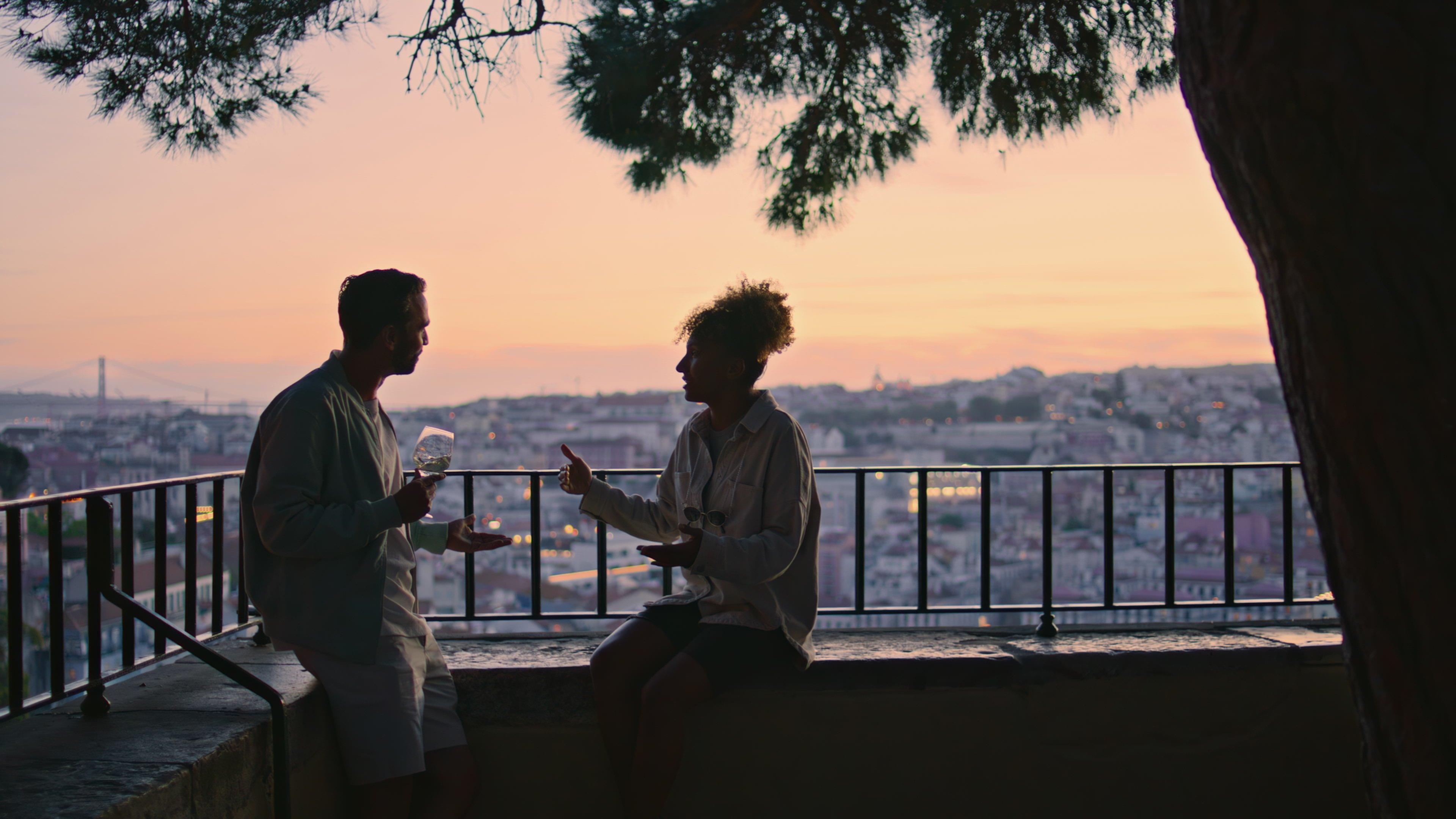 Zwei Menschen sitzen bei Sonnenuntergang im Gespräch auf einer Dachterrasse