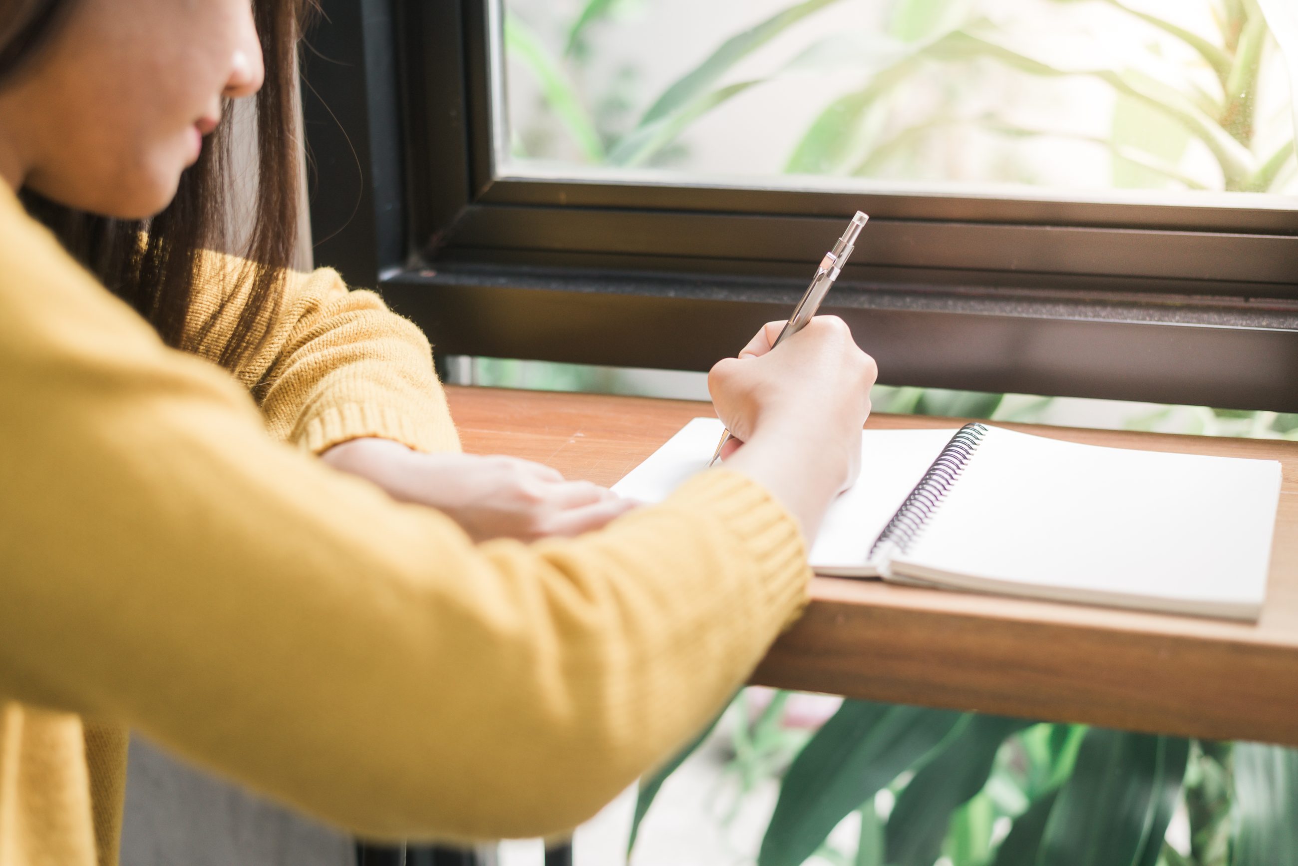 Frau schreibt konzentriert Notizen in ein Notizbuch im warmen Fensterlicht