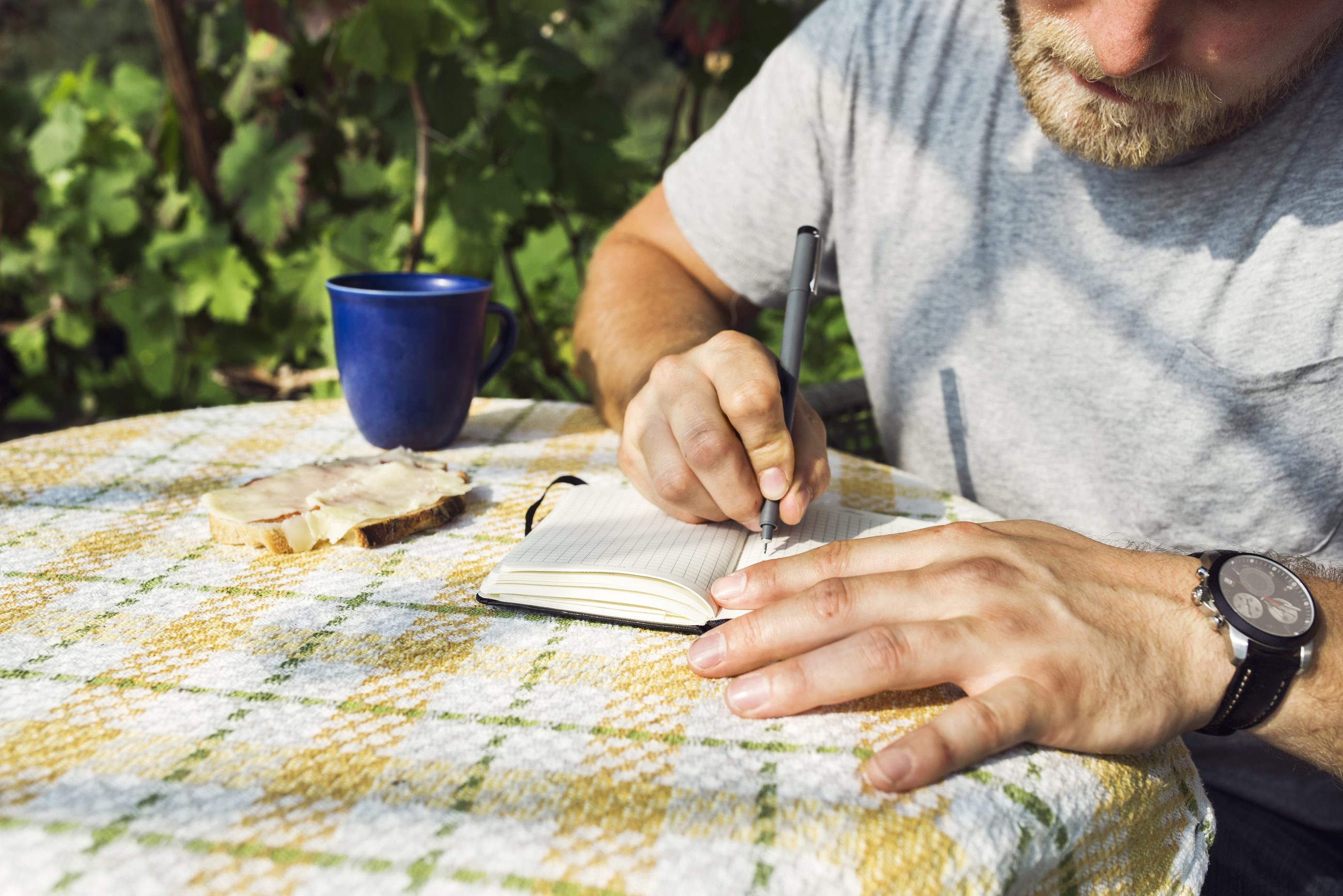 Mann schreibt konzentriert in sein Notizbuch am Morgen im Freien