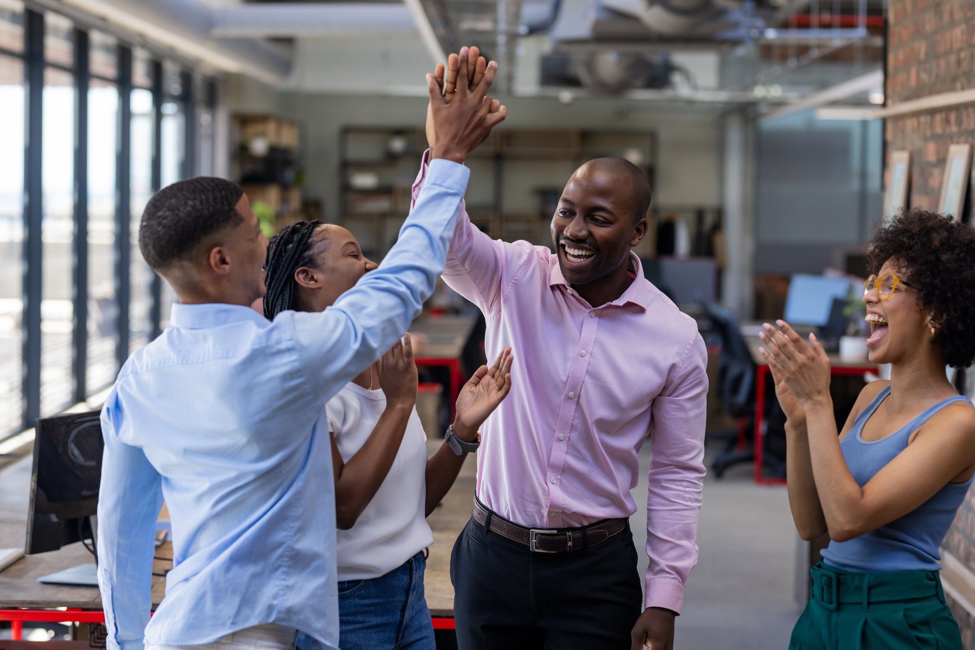 Diverses Team feiert einen gemeinsamen Erfolg mit High Fives im Büro