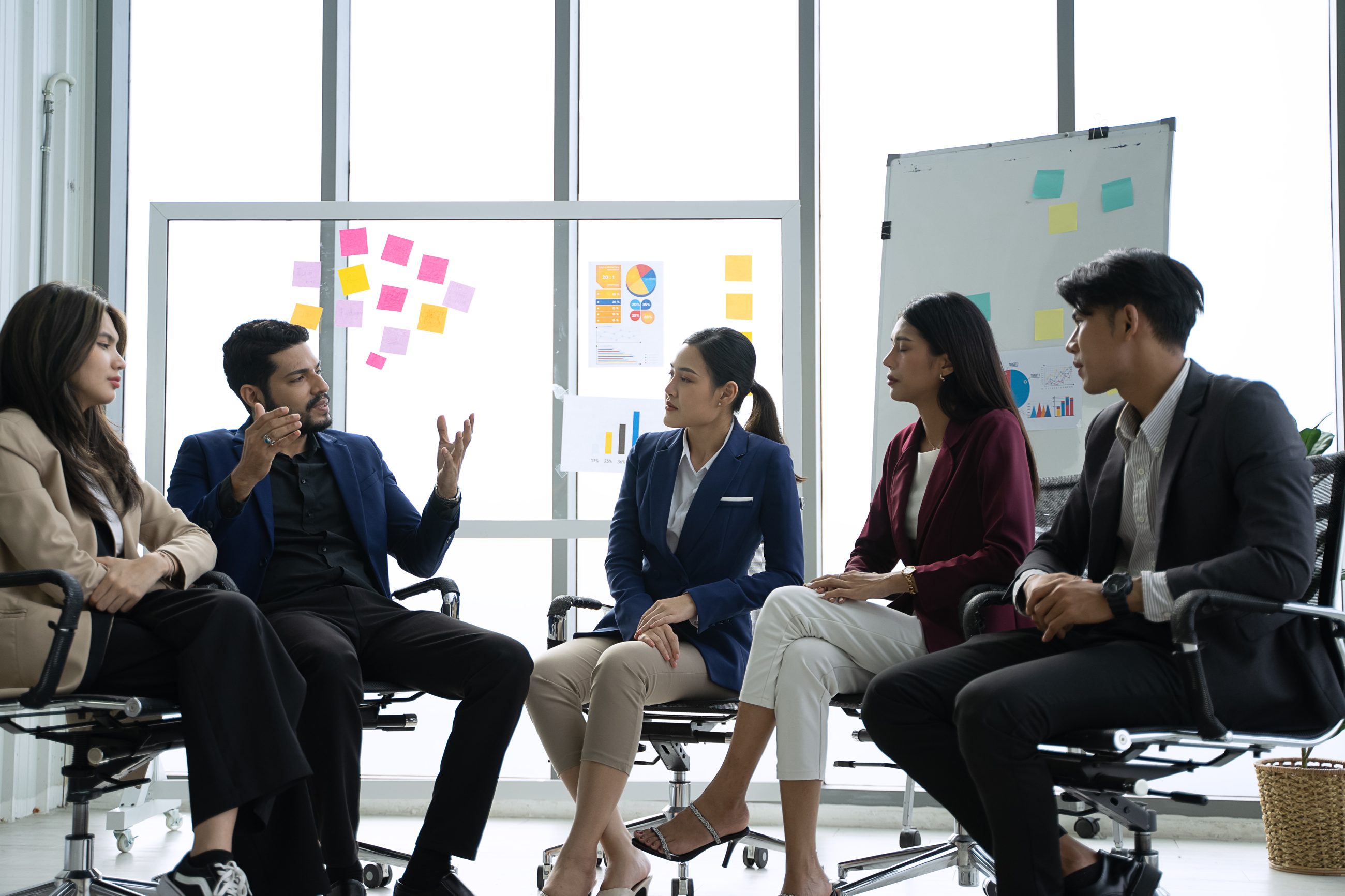 Fünf Teammitglieder diskutieren im Stuhlkreis in einem Workshop zur Teamentwicklung, dahinter Haftnotizen an der Glaswand