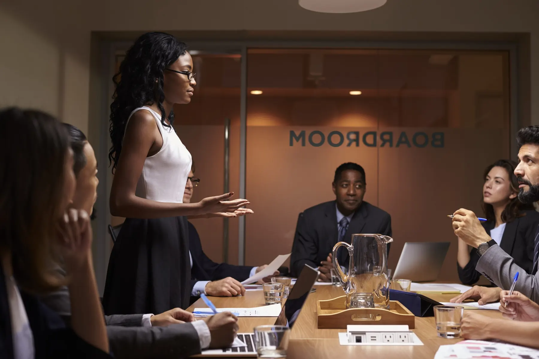 Führungskraft steht im Boardroom-Meeting und bezieht vor dem Team klar Position, Sinnbild für souveräne Kommunikation und Executive Presence