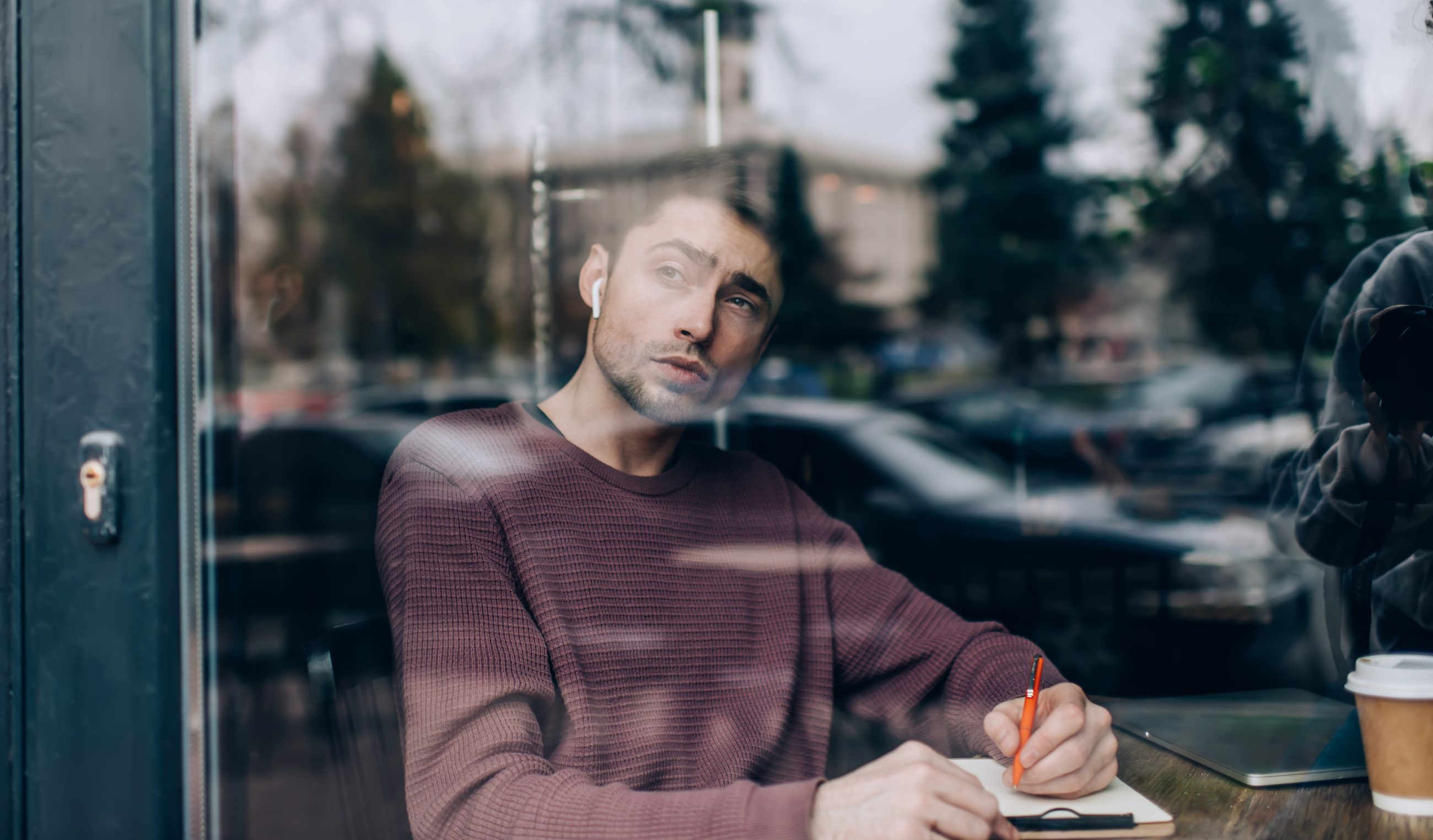 Mann notiert sein Urteil in ein Notizbuch am Caféfenster, Sinnbild für eigenständiges Denken trotz Mehrheitsmeinung