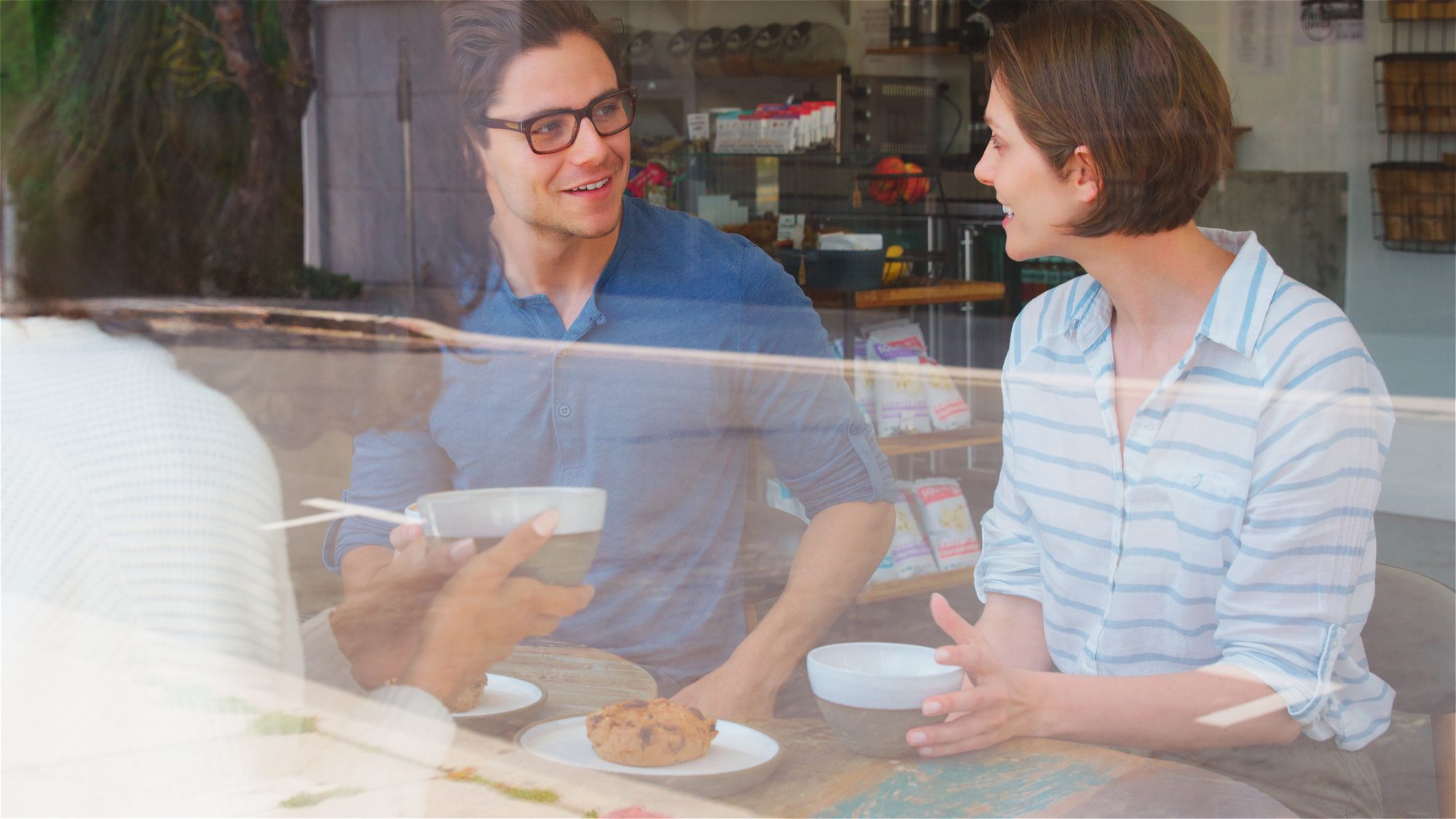 Zwei Menschen unterhalten sich hinter der spiegelnden Fensterscheibe eines Cafés, Sinnbild für den Mere-Exposure-Effekt, bei dem wiederholte Begegnung Sympathie erzeugt