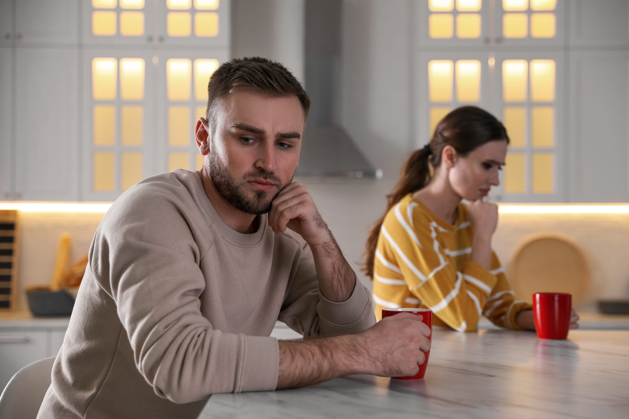 Paar sitzt schweigend am Küchentisch, er stützt den Kopf in die Hand, sie blickt weg, Sinnbild für das Fordern-Rückzug-Muster beim Silent Treatment