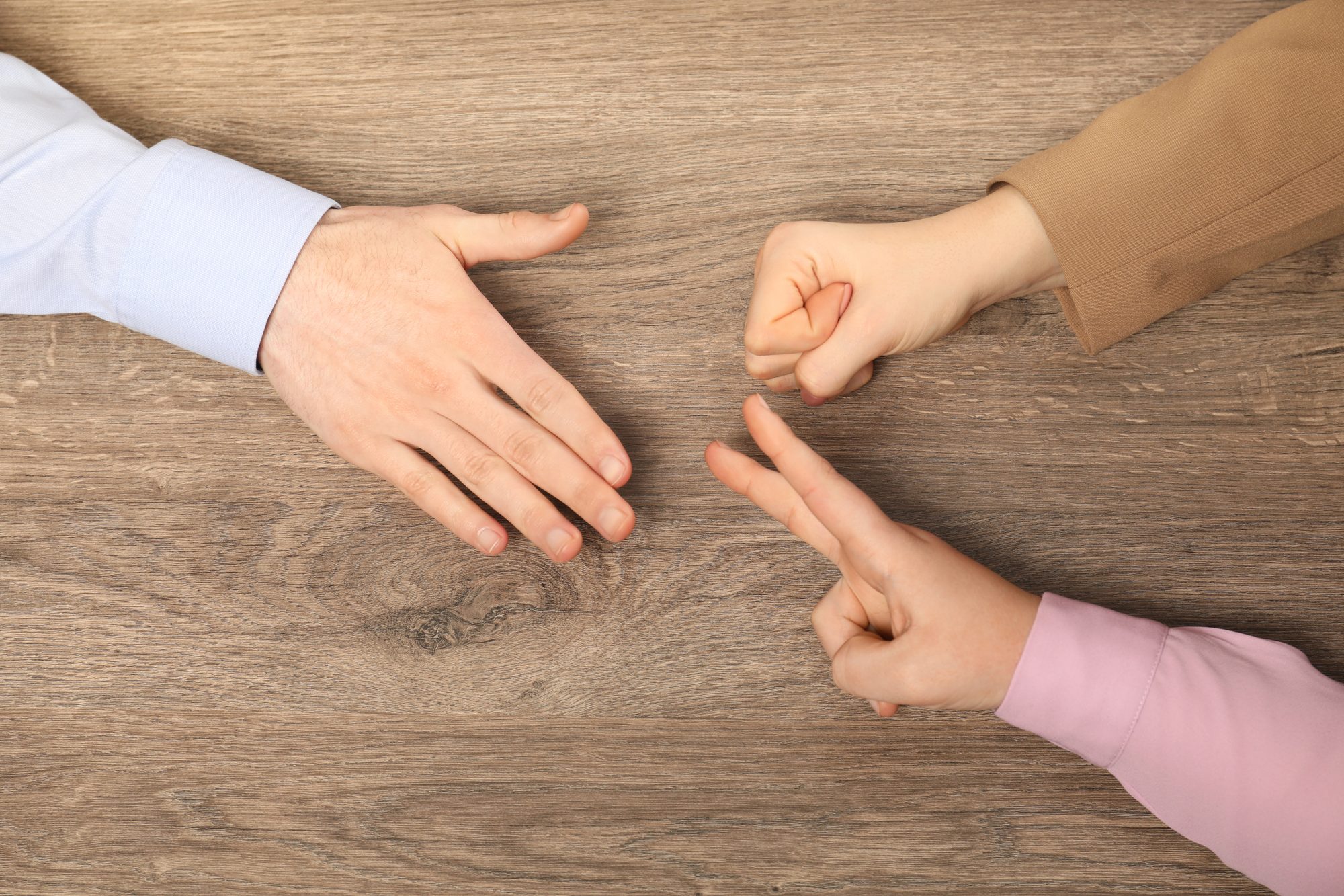 Zwei Hände zeigen auf einem Holztisch mit dem Finger aufeinander, Sinnbild für die Verfolgerrolle im Dramadreieck, in der jeder dem anderen die Schuld gibt