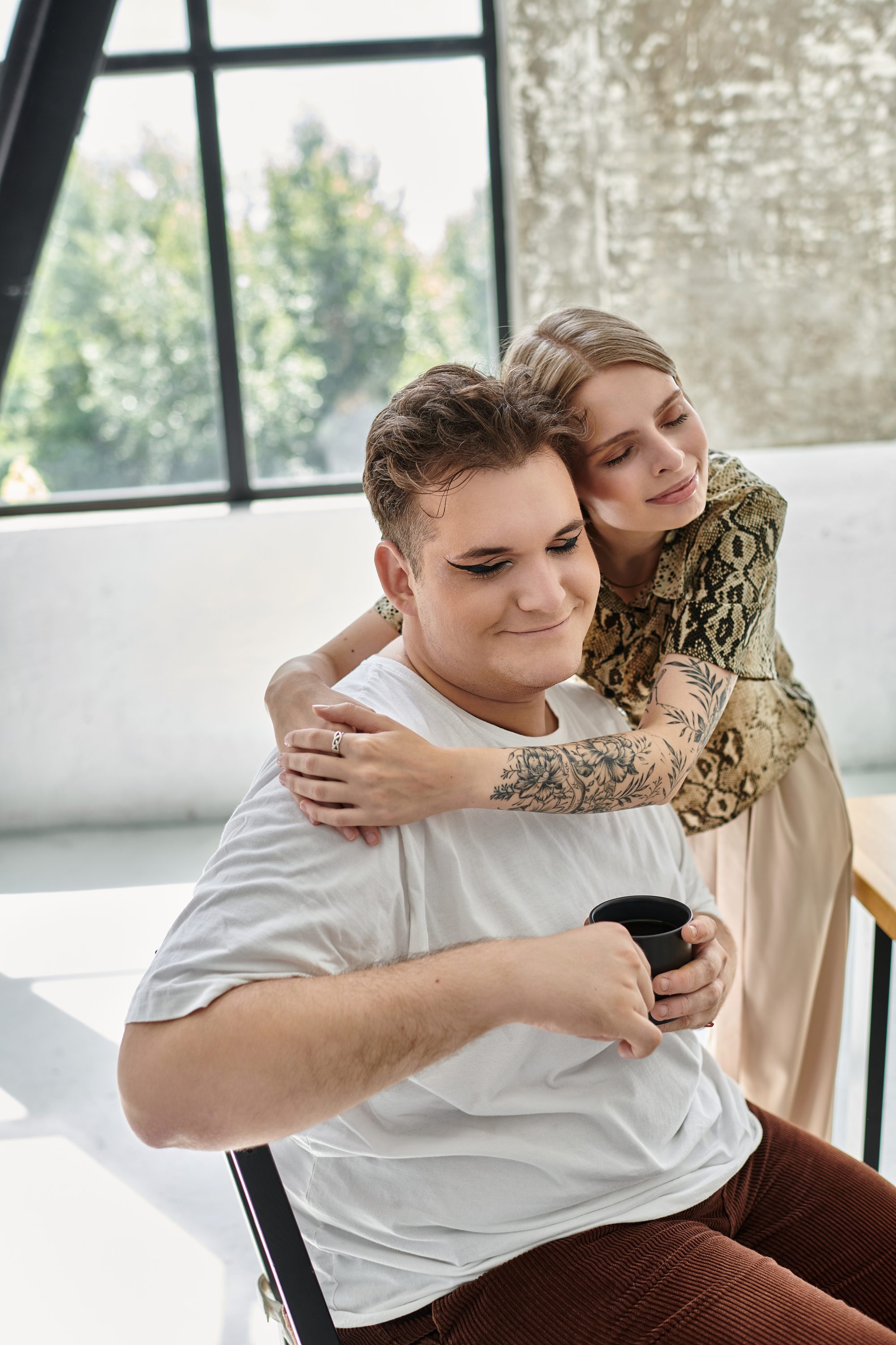 Frau umarmt ihren Partner von hinten, während er abgewandt auf sein Handy schaut, Sinnbild für die Anxious-Avoidant-Falle beim Nähe-Distanz-Problem