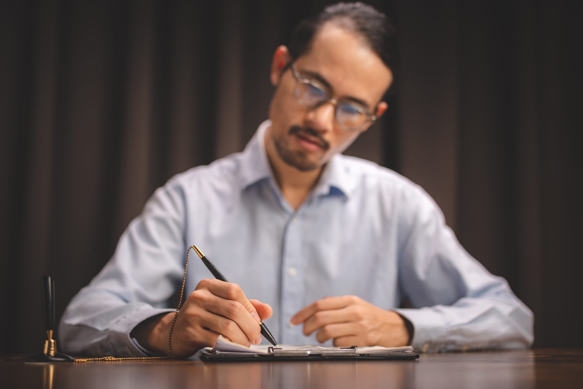 Mann mit Brille schreibt konzentriert mit Füller in ein Notizbuch an einem dunklen Holzschreibtisch, Sinnbild für das Prognosetagebuch gegen Overconfidence