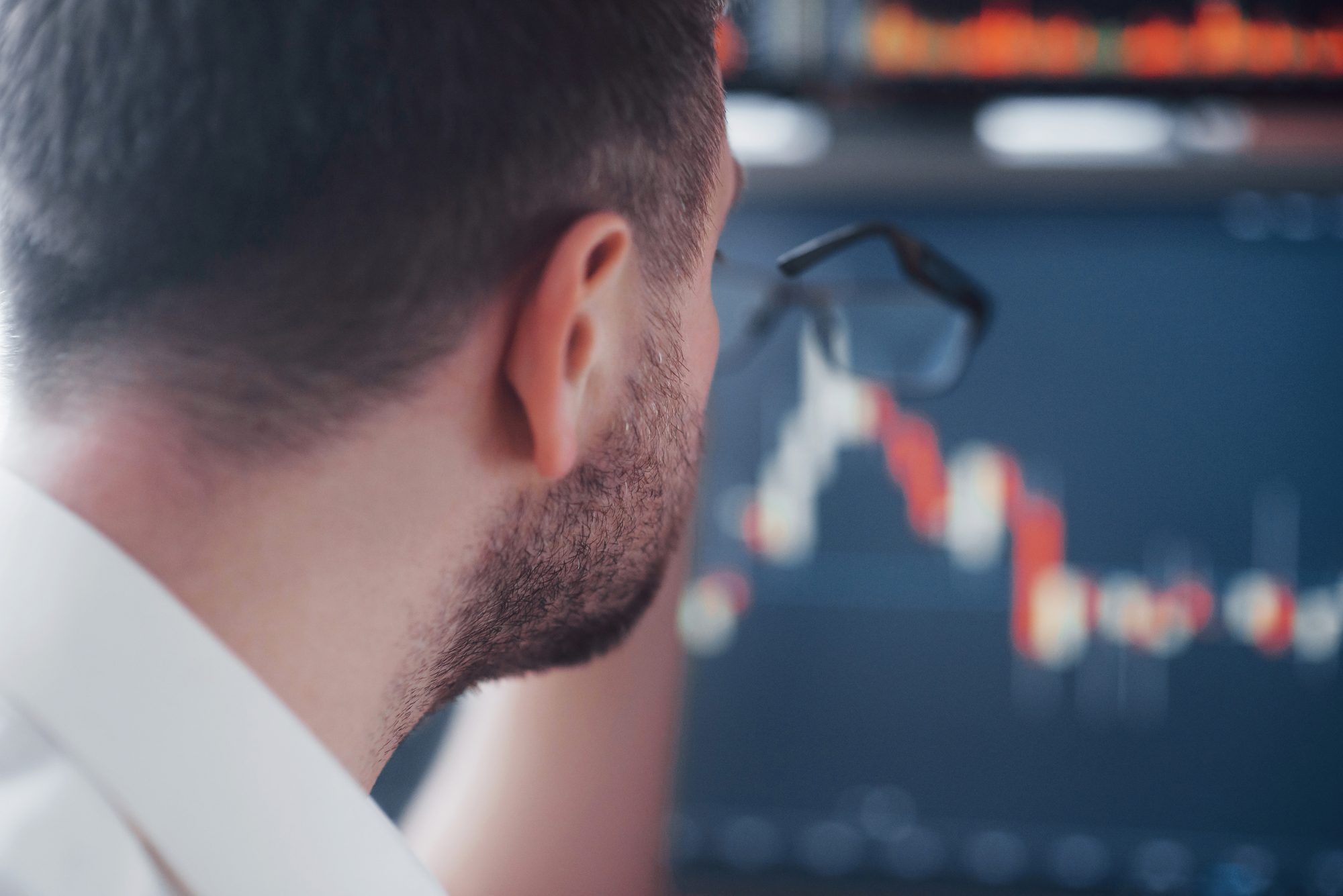 Manager blickt von hinten auf einen Bildschirm mit Börsenkursen, Sinnbild für CEO-Overconfidence und die Überschätzung eigener Investitionsentscheidungen