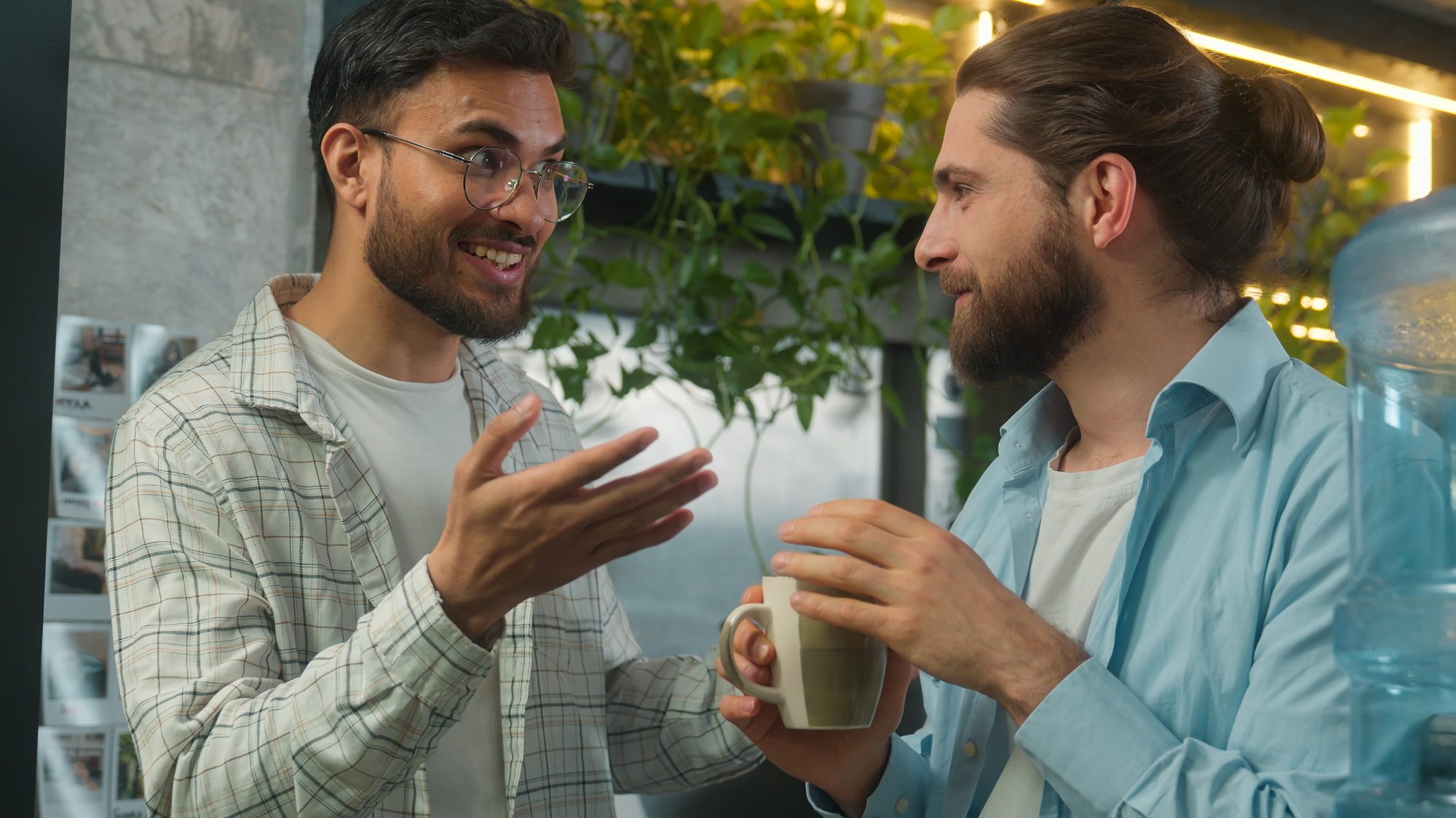 Zwei Männer im Gespräch am Wasserspender im Büro, einer hört aufmerksam zu, Sinnbild für Führungskräfte, die Mitarbeiter souverän beraten und bei eigenen Entscheidungen befangen bleiben