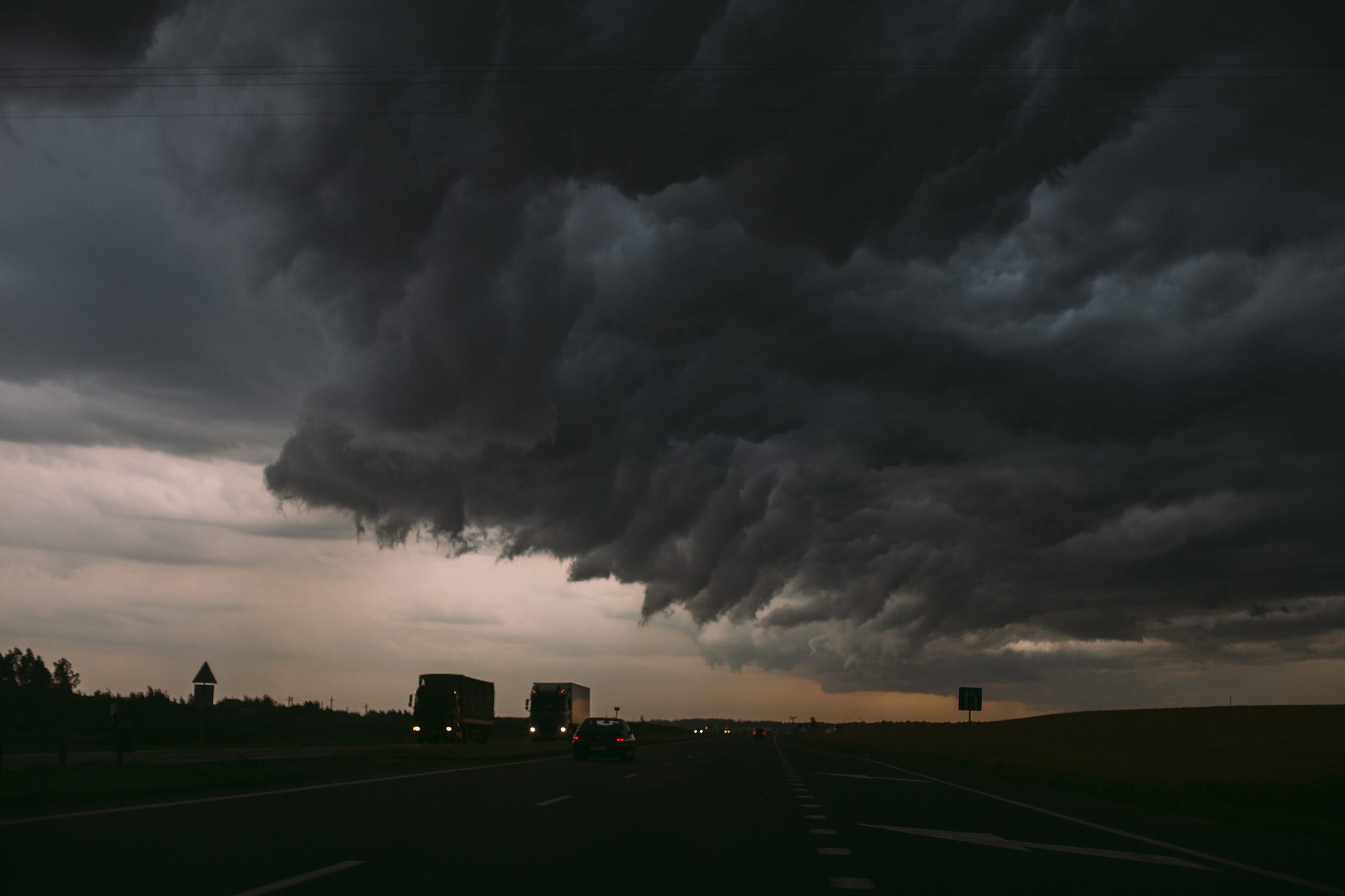 Dunkle Gewitterwolken ziehen über einer Landstraße auf, Sinnbild für die Warnung, die alle sehen könnten und die niemand hören will