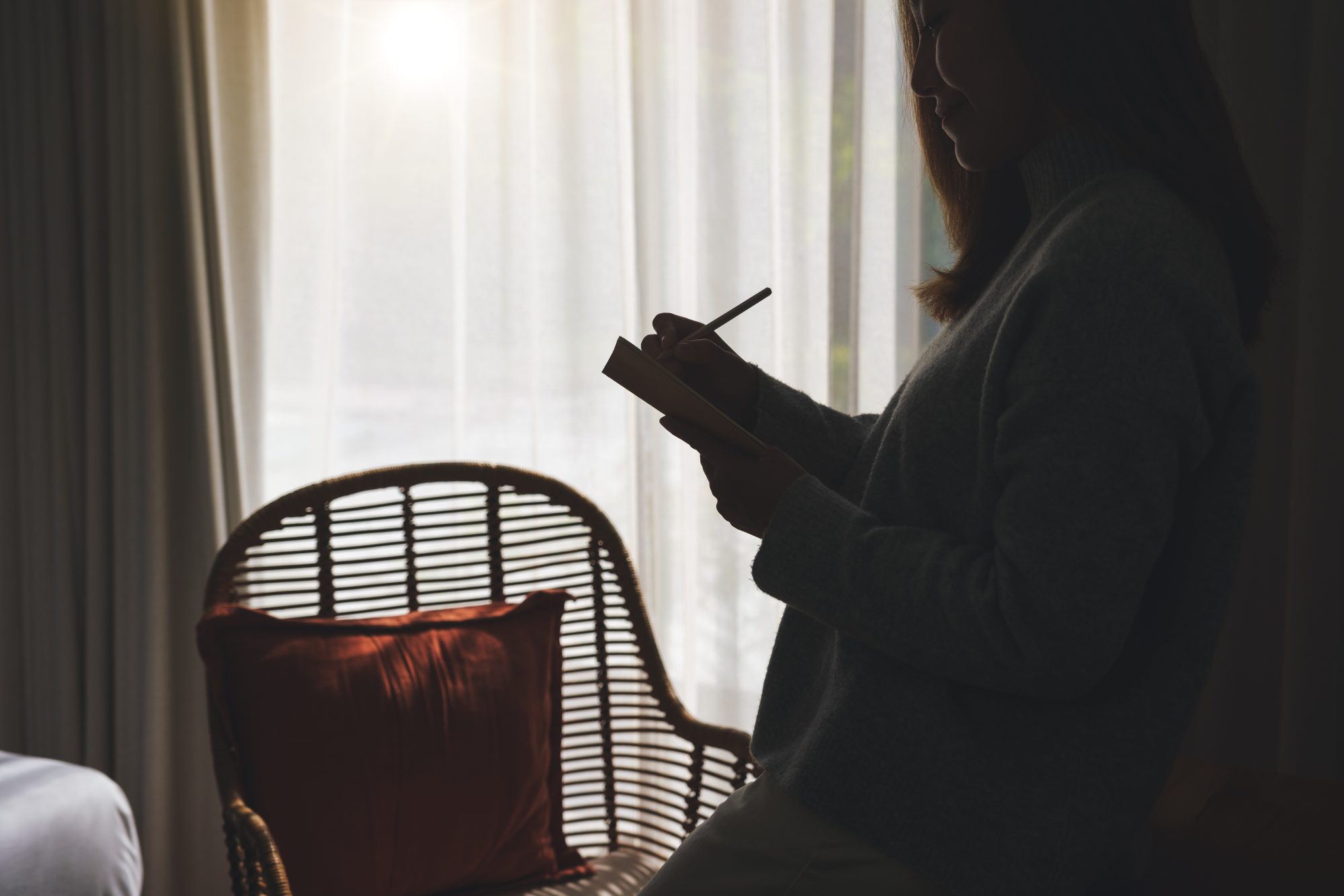 Silhouette einer Frau, die im Fensterlicht in ein Notizbuch schreibt, Sinnbild für das Archiv als Übung zur Objektkonstanz