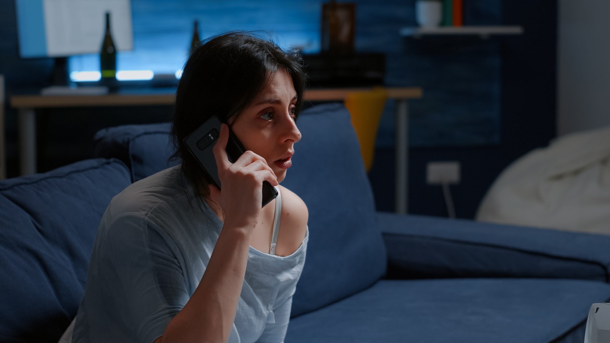 Frau telefoniert abends besorgt auf dem Sofa, Sinnbild für gemeinsames Grübeln am Telefon