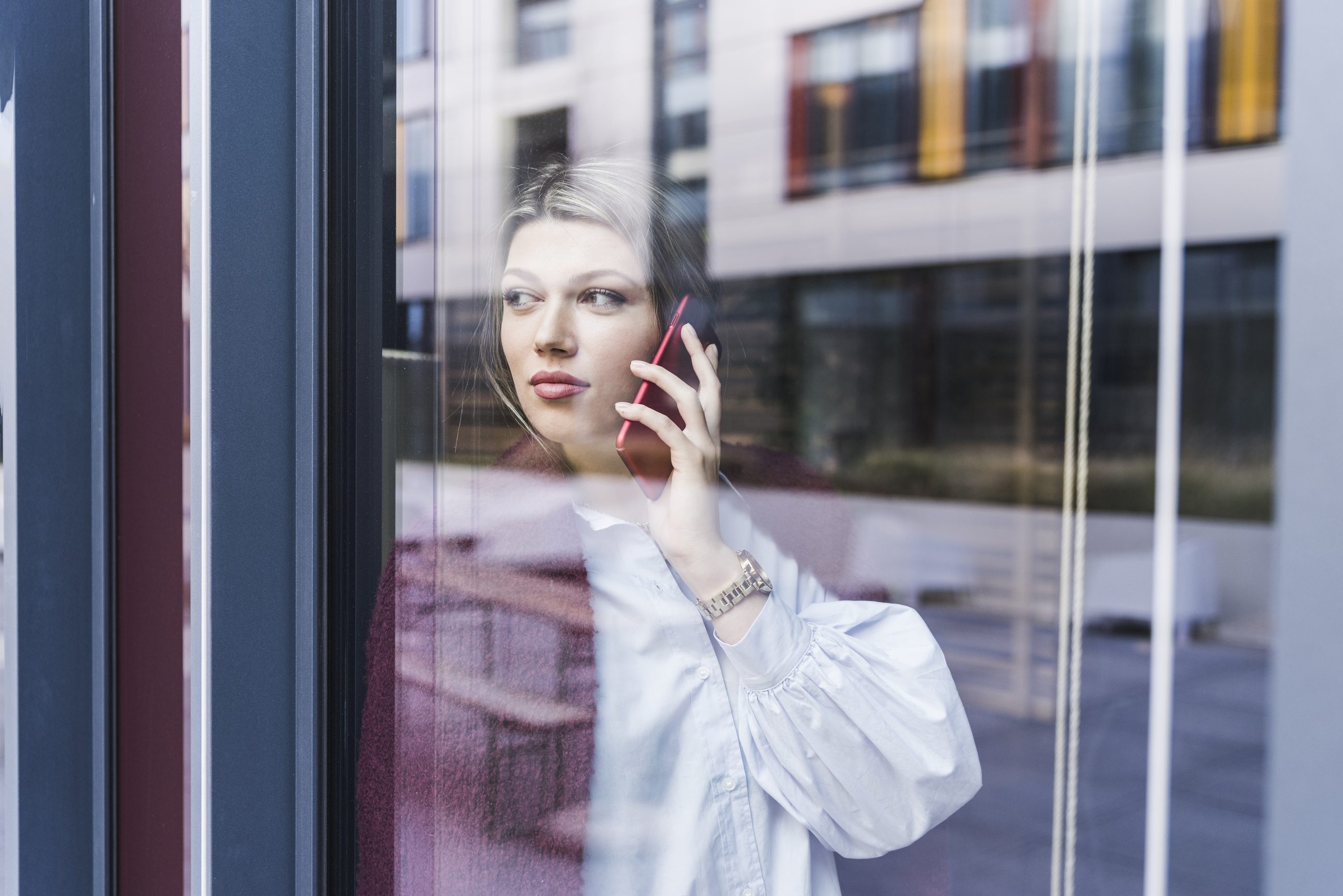 Frau telefoniert hinter einer Fensterscheibe mit ruhigem Gesichtsausdruck, Beispiel für Grey Rock in einem provozierenden Gespräch