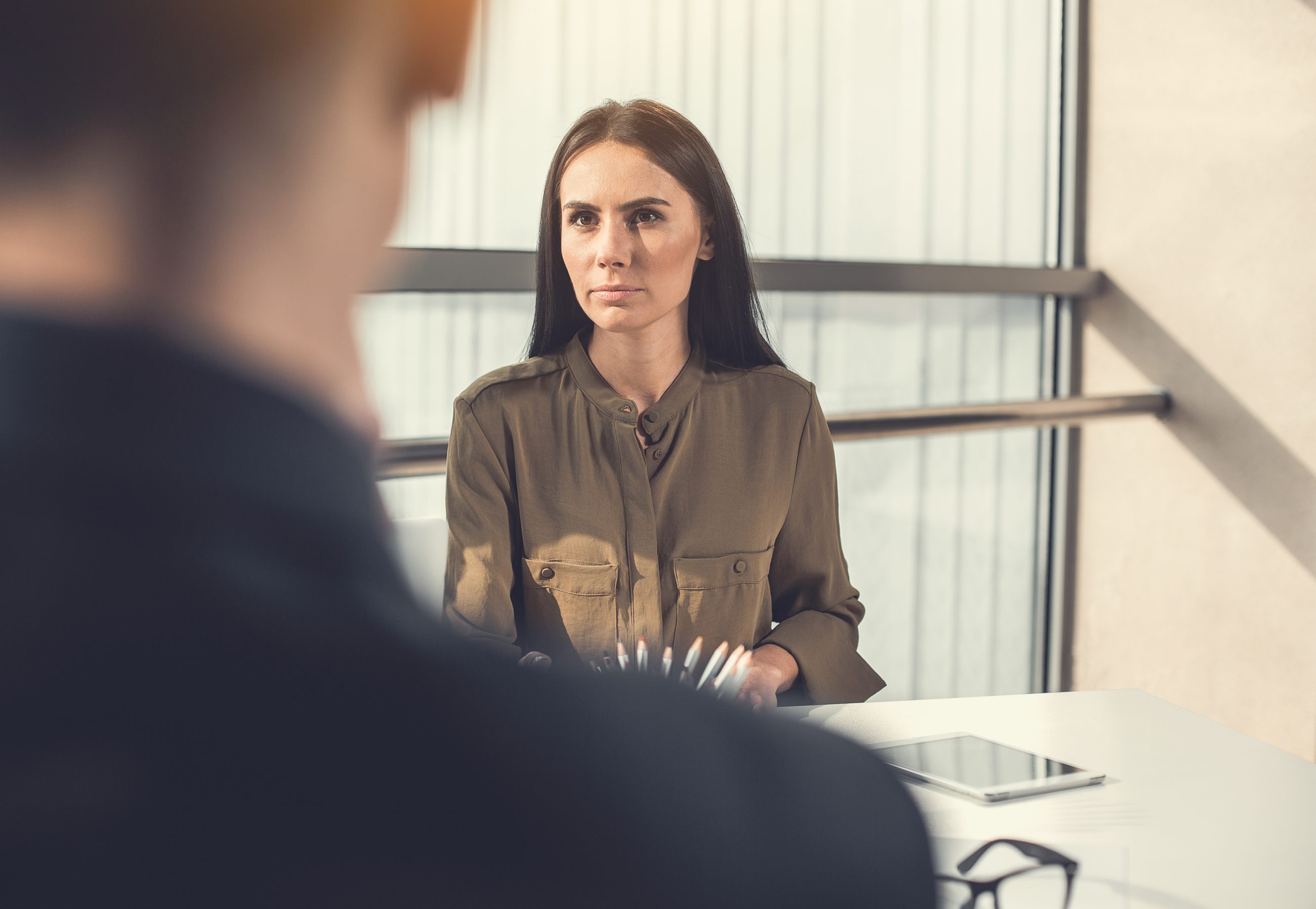 Kandidatin sitzt ernst im Vorstellungsgespräch gegenüber einem Interviewer, Sinnbild für den Outcome Bias bei der Auswahl nach Track Record
