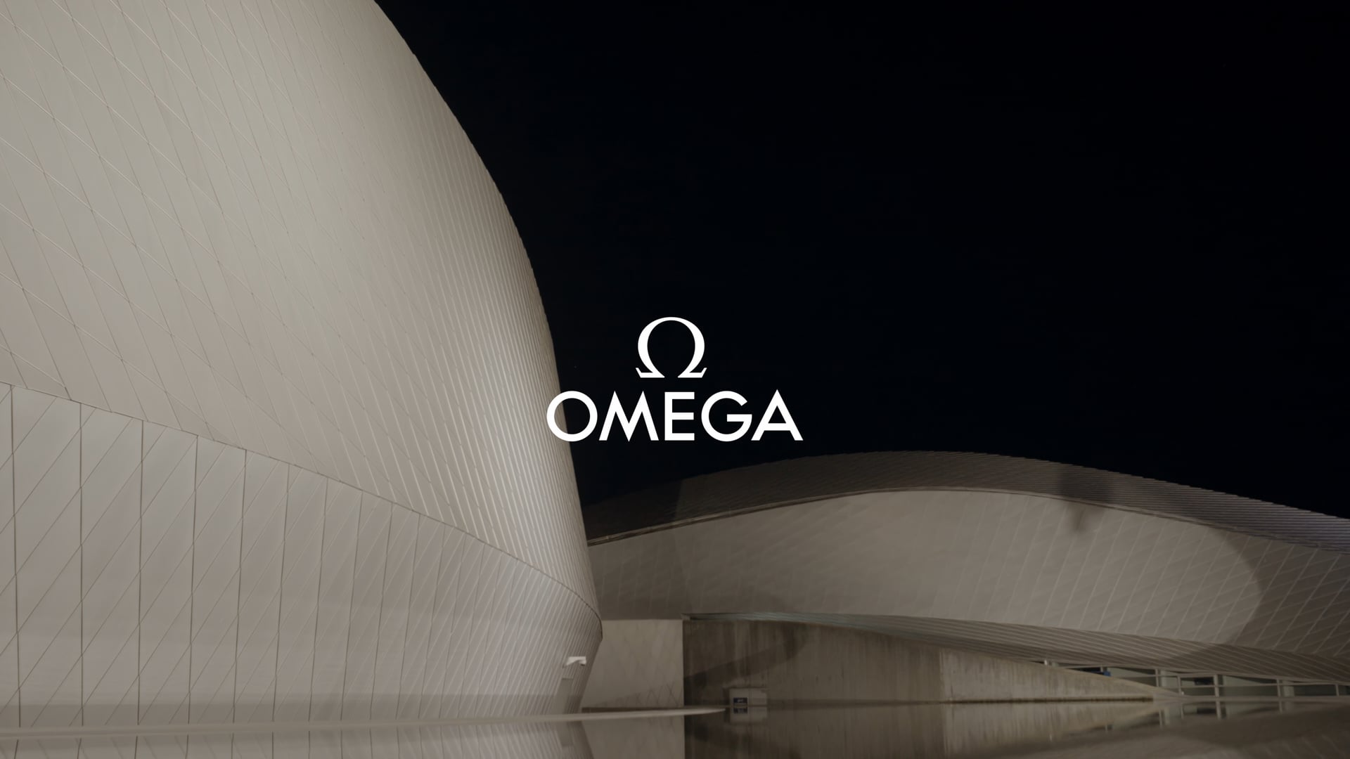 OMEGA-logoet over Den Blå Planets facade ved aftenstid – åbningsbilledet fra Planet Ocean-lanceringen