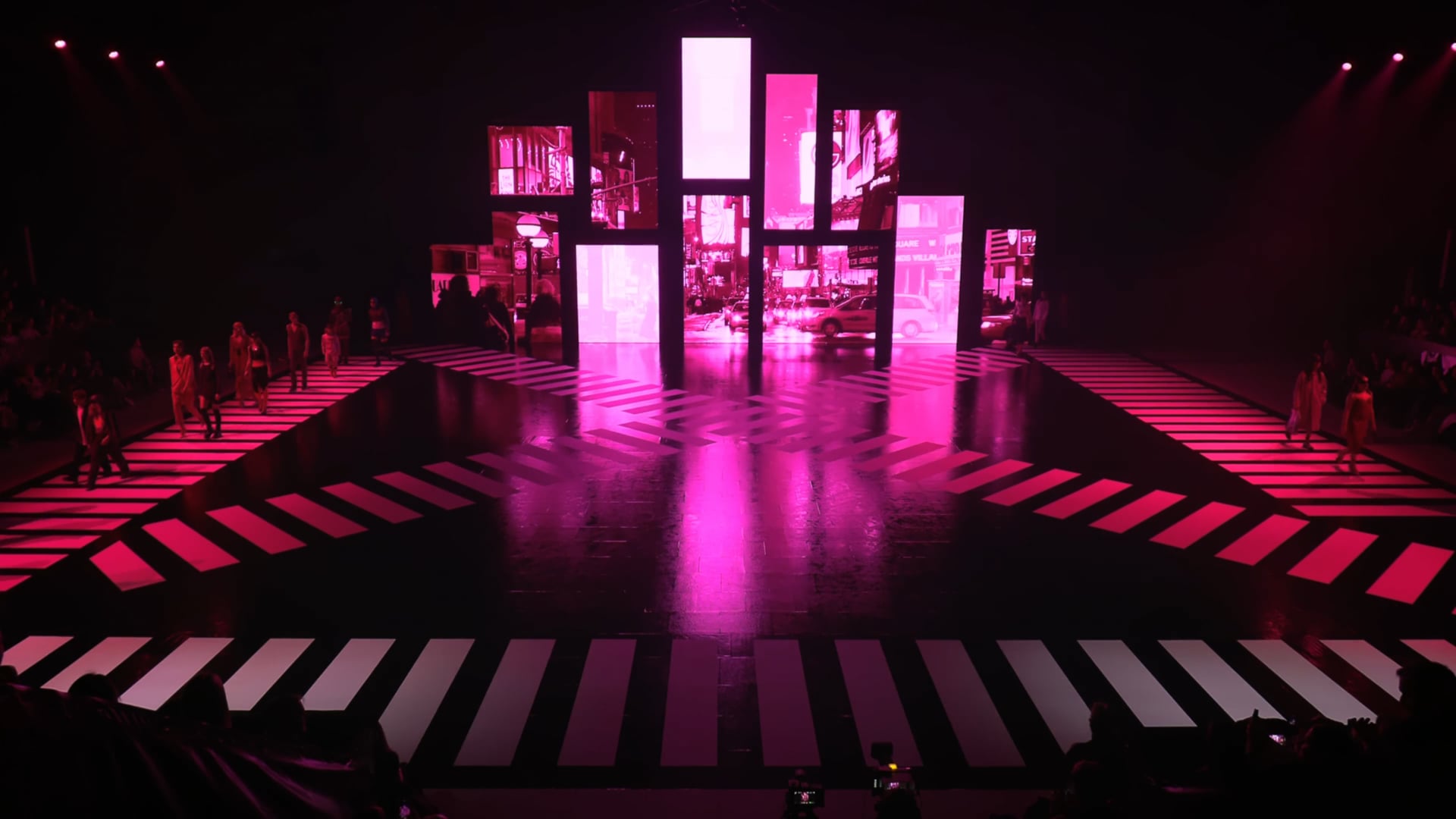 Catwalk bygget som et fodgængerfelt-kryds i pink lys, hvor modeller går mellem høje LED-skærme med en bygade