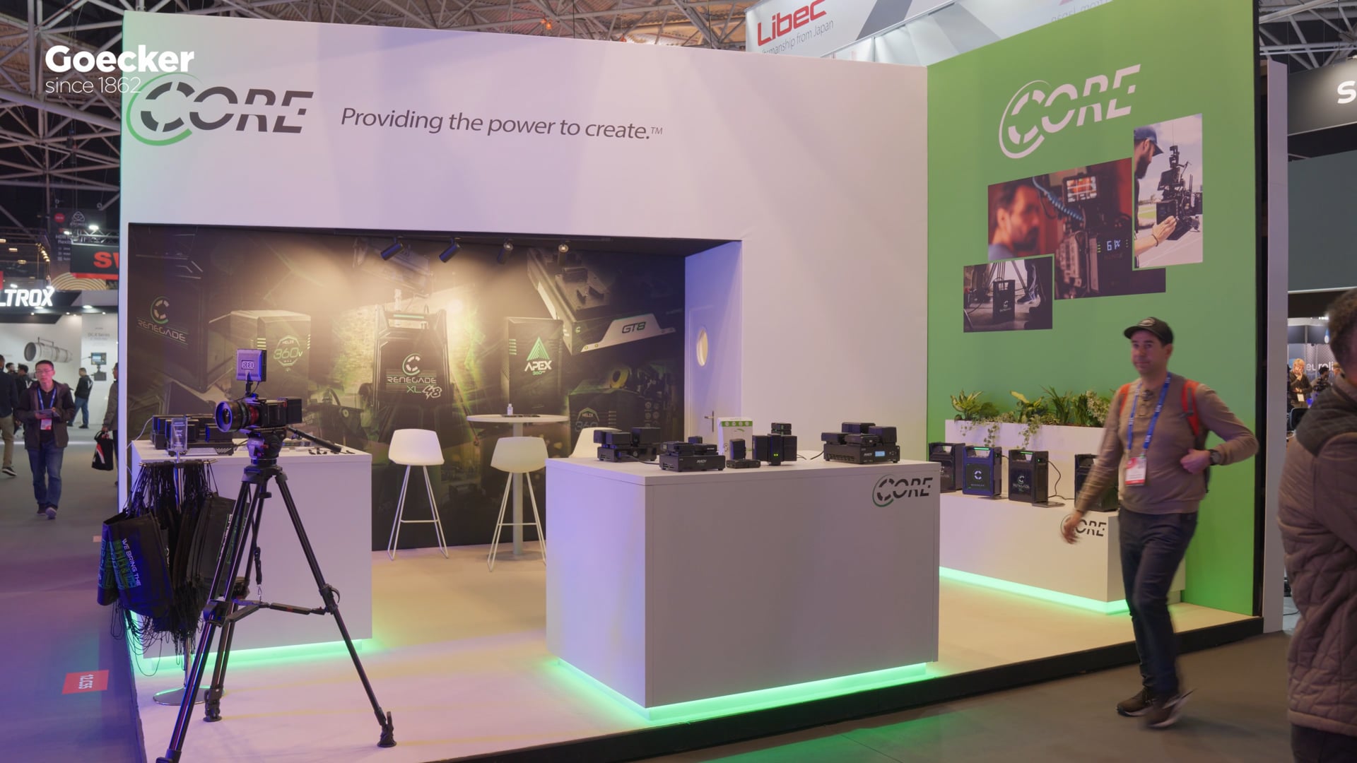Core SWX-standen på IBC-messen i Amsterdam med grøn standbelysning, udstillede batterier og messegæster, med Goecker-logo i hjørnet