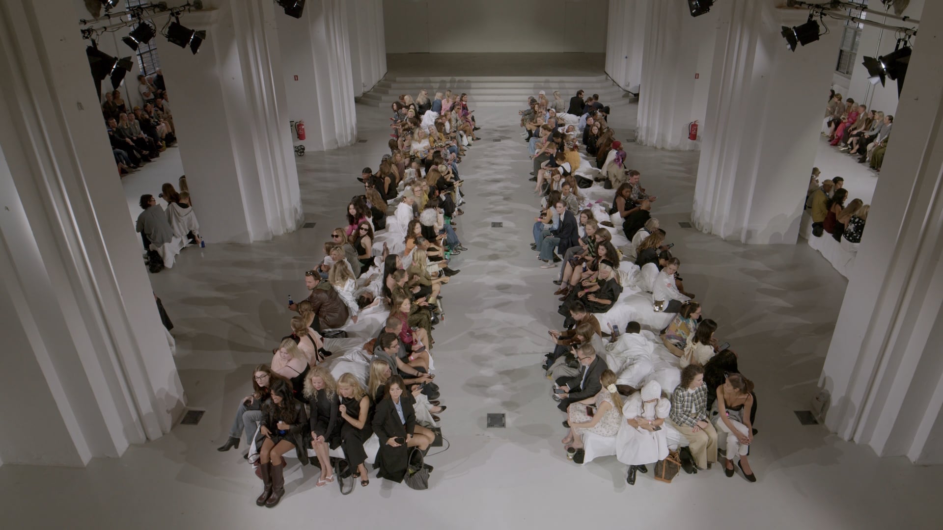Catwalk set oppefra i Nikolaj Kunsthal med publikum siddende på begge sider af den hvide løber