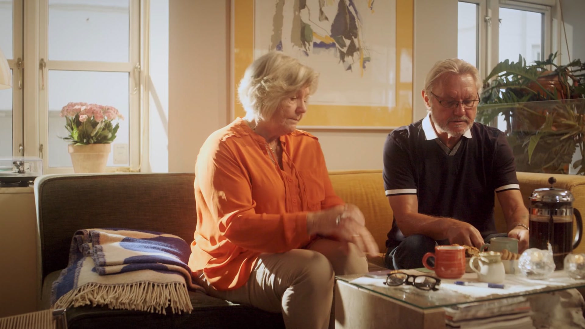 Ældre par sidder i sofaen med kaffe og samtalekort på bordet i Det Gode Testamentes kampagnefilm
