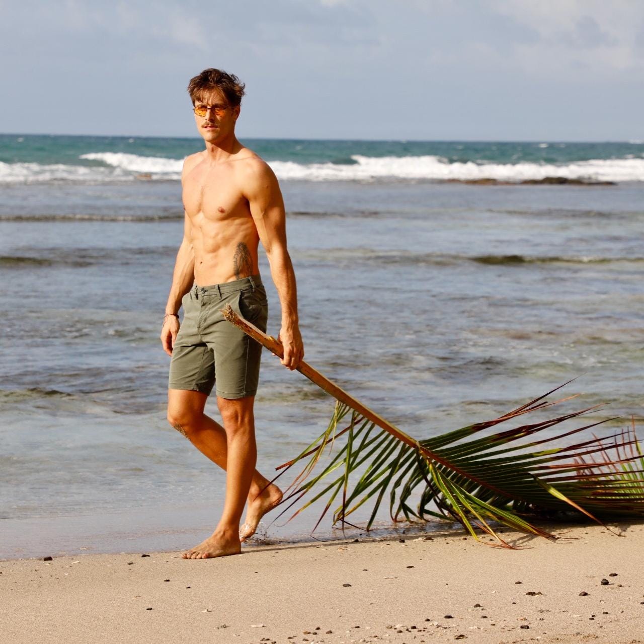 Taylor Rice standing on a beach holding a palm frond