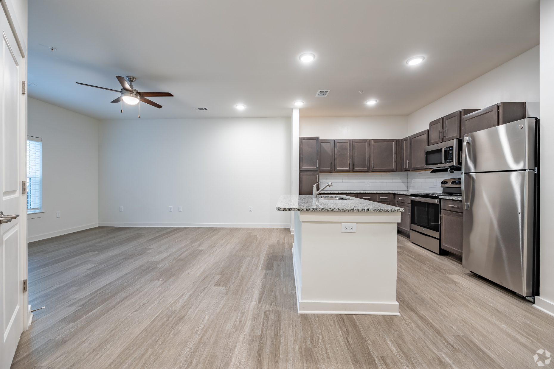 Wide view of unfurnished living area and kitchen with island and stainless steel appliances