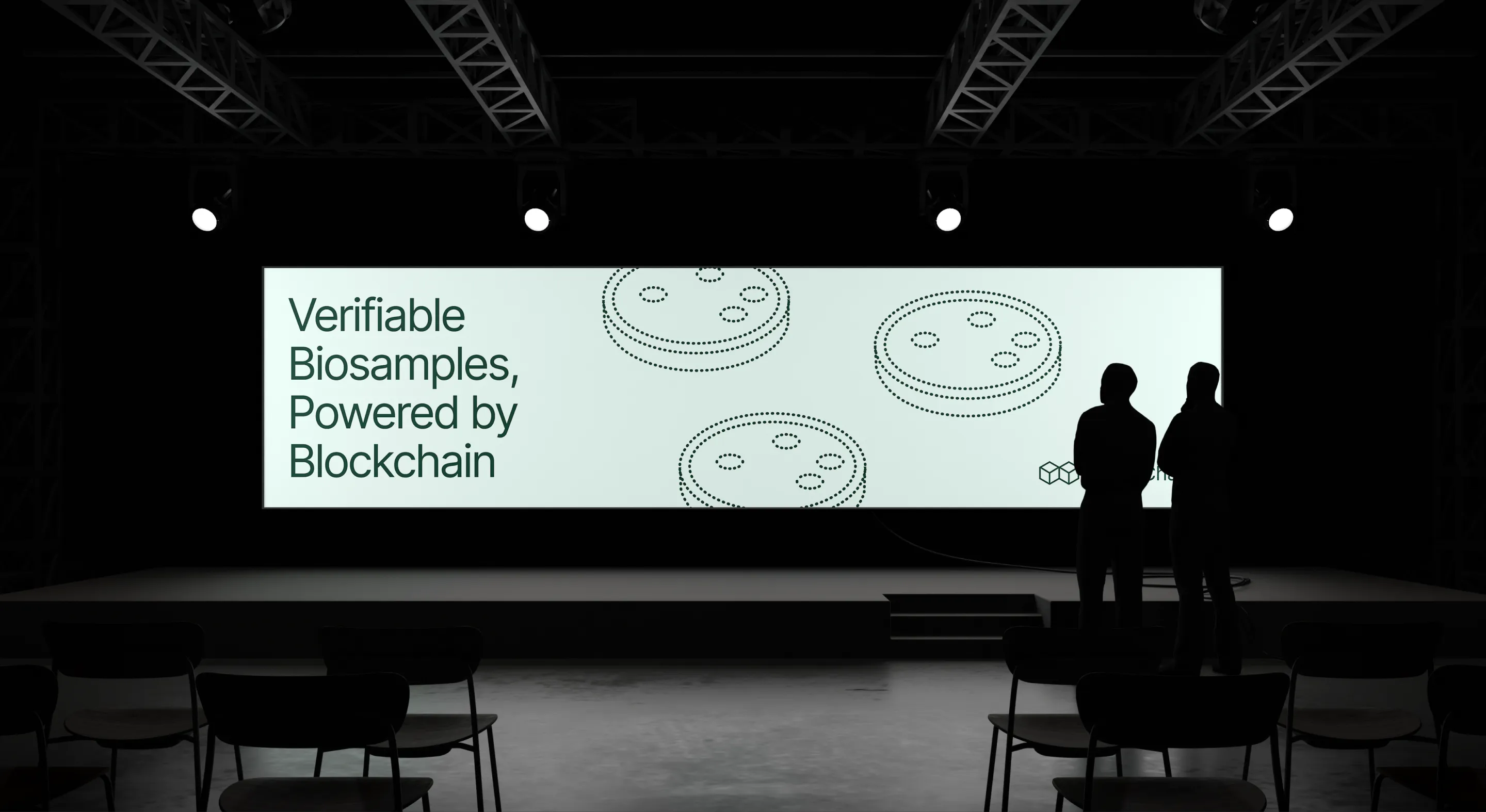 Stage with large screen reading ‘Verifiable Biosamples, Powered by Blockchain’ and two silhouetted figures.