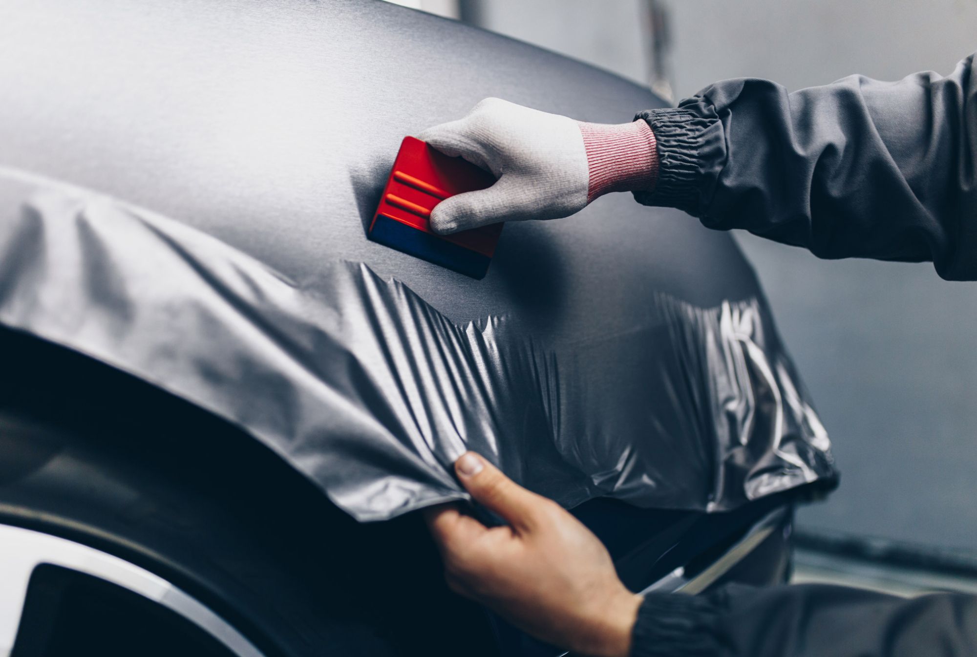 Facharbeiter trägt mit einer Rakel eine silbergraue Autofolie auf eine Fahrzeugkarosserie auf