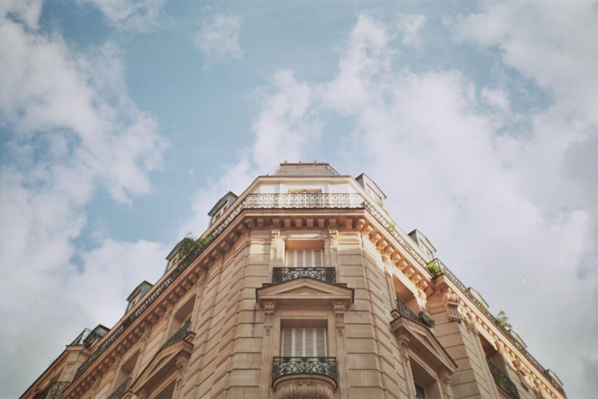 Façade d’un immeuble haussmannien parisien vue depuis la rue, sous un ciel nuageux