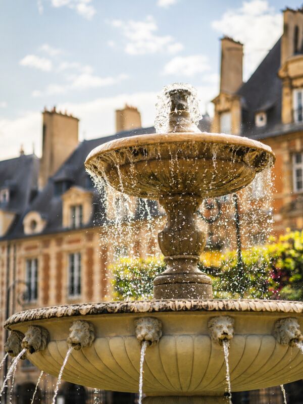 Fontaine en pierre dans la Place des Vosges à Paris, entourée d’édifices historiques