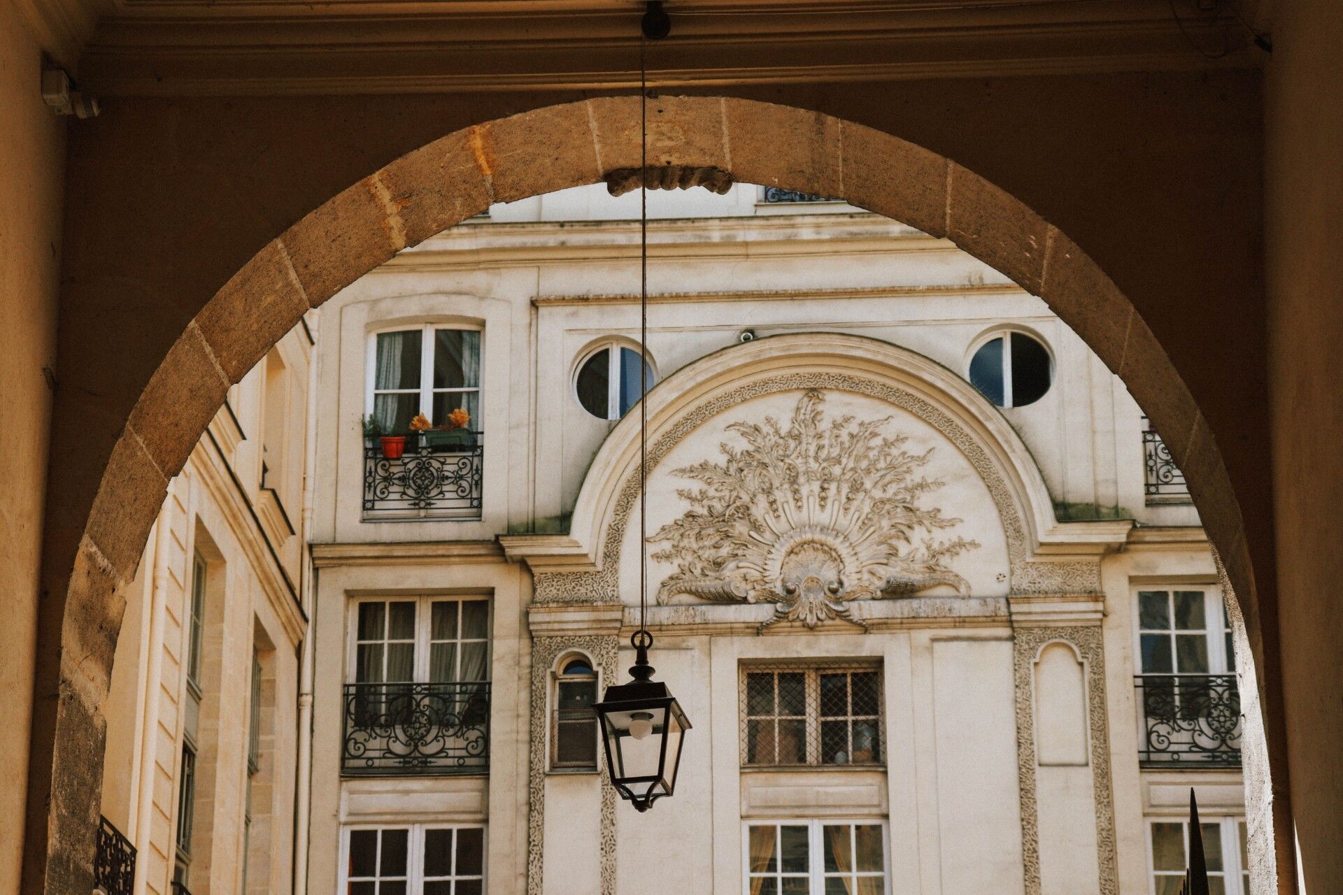 Vue sur une façade parisienne ornée depuis une cour intérieure, à travers une arche en pierre