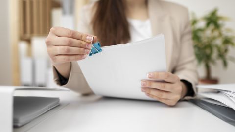 Une femme en tenue professionnelle assemble des documents à l’aide d’une pince bleue.