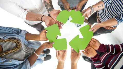 Un groupe de personnes tient ensemble le symbole vert du recyclage, représentant un engagement collectif pour l’environnement.