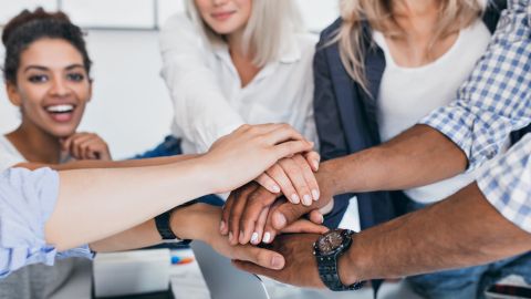 Une équipe souriante réunit ses mains au centre pour symboliser la cohésion et l’engagement collectif.