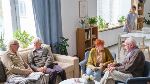 Des résidents échangent paisiblement dans le salon d’un établissement, sous le regard d’une soignante.