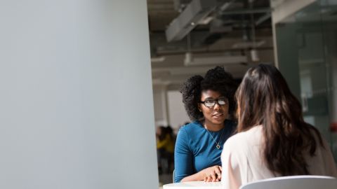 Deux femmes échangent face à face dans un bureau lumineux, dans une atmosphère professionnelle.
