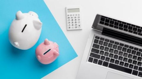 Deux tirelires et une calculatrice sont posées près d’un ordinateur, symbolisant la gestion financière.