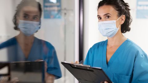Une soignante masquée tient un dossier et effectue un suivi dans un service médical.
