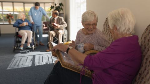 Cette image montre des personnes âgées dans une maison de retraite, en train de regarder des photos ensemble.