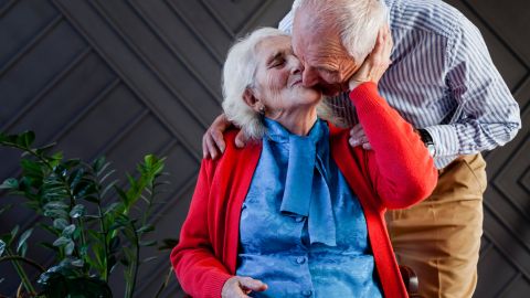 Couple de personnes âgées s'embrasse tendrement. Madame est assise et monsieur se penche pour l'embrasser.