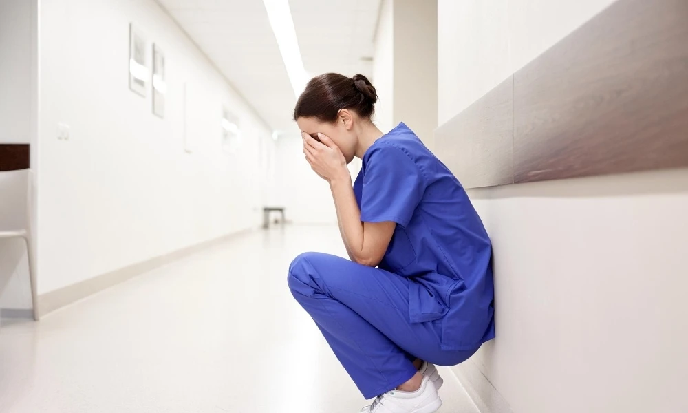 Professionnel de santé qui est accroupi contre un mur se tenant la tête avec les mains